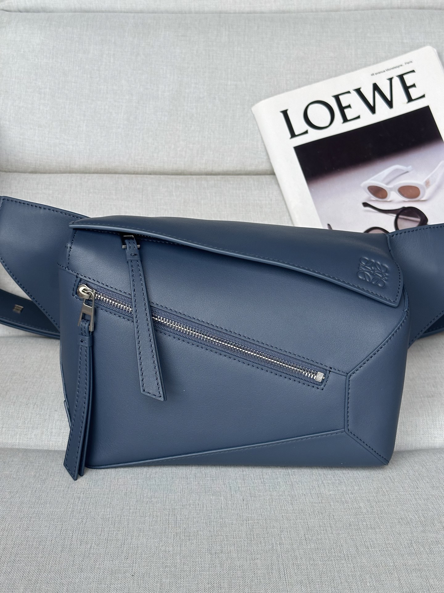 NO:341128,Extra Classic Cowhide Puzzle Puzzle 6003 Indigo Puzzle handbag is the first tote for LOEWE by creative director Jonathan Anderson. The rectangular shape and precise cutting technology create the unique geometric lines of Puzzle. This small waistbag is made of classic cowhide leather with overlapping edges. Shoulder or crossbody Adjustable shoulder straps with metal buckle closure engraved with LOEWE logo Zip closure, cowhide zipper head External zipper pocket and interior insert pocket Herringbone cotton canvas lining Anagram embossed 24-10.5-16, Extra Classic Loewe, loewe, loewe, cowhide19860909特级 小号经典牛皮革 Puzzle 腰包 6003 靛蓝 Puzzle 手袋是创意总监乔纳森·安德森（Jonathan Anderson）为 LOEWE 推出的首款手提包.长方体形状和精确的切割技术创造了 Puzzle 独特的几何线条.这款小号腰包采用经典牛皮革制成,饰有重叠边缘. 可肩背或斜挎 可调节肩带配有金属搭扣开合,刻有 LOEWE 徽标 拉链开合,牛皮革拉链头 外部拉链口袋和内部插袋 人字纹棉质帆布衬里 Anagram 压纹 24-10.5-16,特级罗意威,loewe,loewe,cowhide,Bag