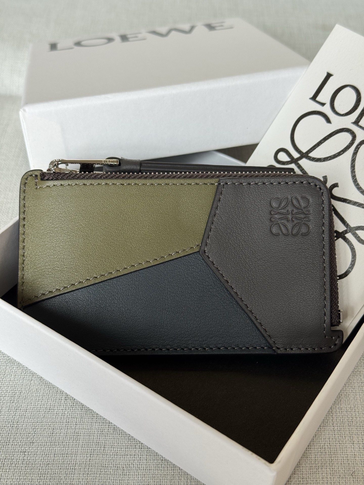 NO:670906,Premium Classic Calf Leather Puzzle Coin Card Holder A03B Olive Green/Coffee This coin card holder is inspired by the Puzzle bag and features a unique geometric pattern. This version is crafted in contrasting classic calfskin. Four card slots One zippered coin compartment, calf leather zipper puller Calf leather lining Anagram embossed cm·in Color Dye Indigo/Heather Metallic color Palladium Gold Main material Classic Calf Leather Weight 0.04  kg Height 7.5 cm Width 13 cm Depth 1 cm, premium Loewe, loewe, cowhide19860909特级 经典牛皮革 Puzzle 硬币卡包A03B 橄榄绿/咖啡 这款硬币卡包的灵感来自 Puzzle 手袋,采用独特的几何图案.此版本采用对比色经典小牛皮制成. 四个卡位 一个拉链硬币隔层,牛皮革拉链头 牛皮革衬里 Anagram 压纹 公分·in Colour 染料靛蓝色/麻灰色 Metallic colour 钯金色 Main material 经典牛皮革 Weight 0.04 kg Height 7.5 公分 Width 13 公分 Depth 1 公分,特级罗意威,loewe,cowhide,Bag