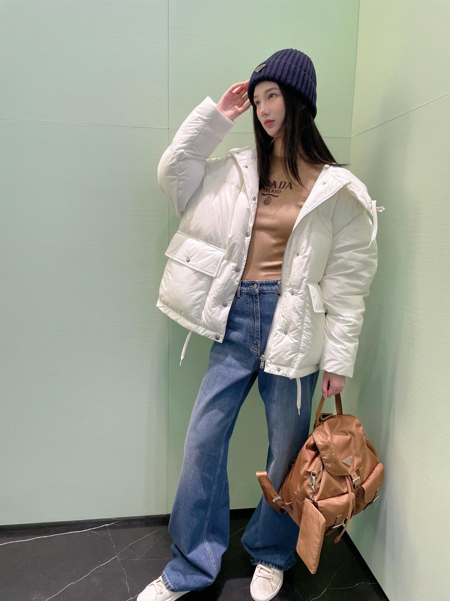 💰批690 🆕Prad* 25Fw秋冬新款 三角徽标白色连帽夹克羽绒服丨⚠独家yb开发！高版出品！采用品牌标志性的 Re-Nylon 再生尼龙面料（由海洋回收塑料净化再生而成），兼具防水功能性与柔和哑光质感，米白色调在秋冬衣橱中更显干净高级；70%鹅绒填充饱满蓬松，连帽带抽绳可调节松紧，下摆抽绳自由控制廓形；双侧大贴袋兼具工装实用性与视觉层次感，日常出行随手置物便利又时髦。现货发售S/M/L
