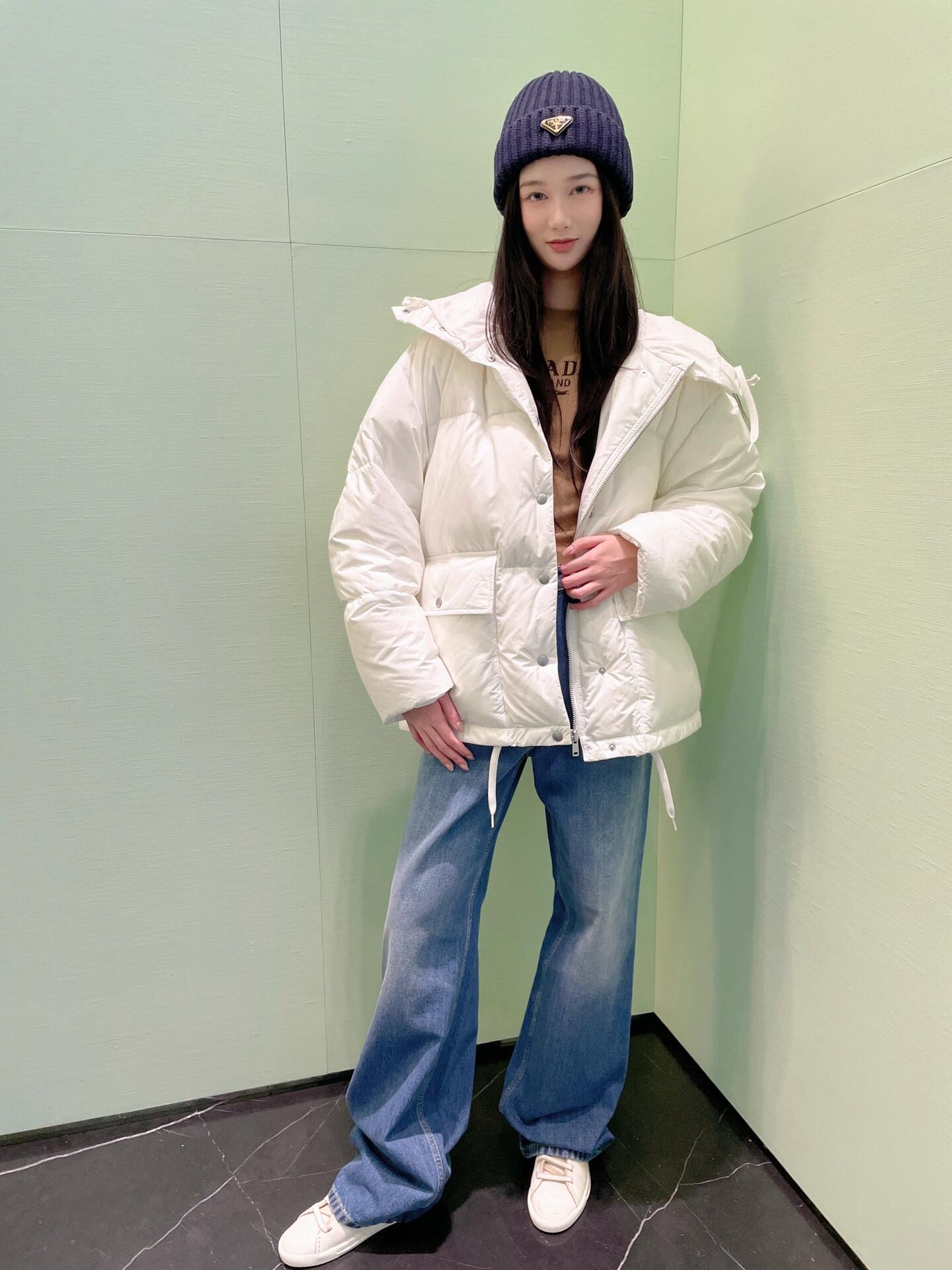 💰批690 🆕Prad* 25Fw秋冬新款 三角徽标白色连帽夹克羽绒服丨⚠独家yb开发！高版出品！采用品牌标志性的 Re-Nylon 再生尼龙面料（由海洋回收塑料净化再生而成），兼具防水功能性与柔和哑光质感，米白色调在秋冬衣橱中更显干净高级；70%鹅绒填充饱满蓬松，连帽带抽绳可调节松紧，下摆抽绳自由控制廓形；双侧大贴袋兼具工装实用性与视觉层次感，日常出行随手置物便利又时髦。现货发售S/M/L