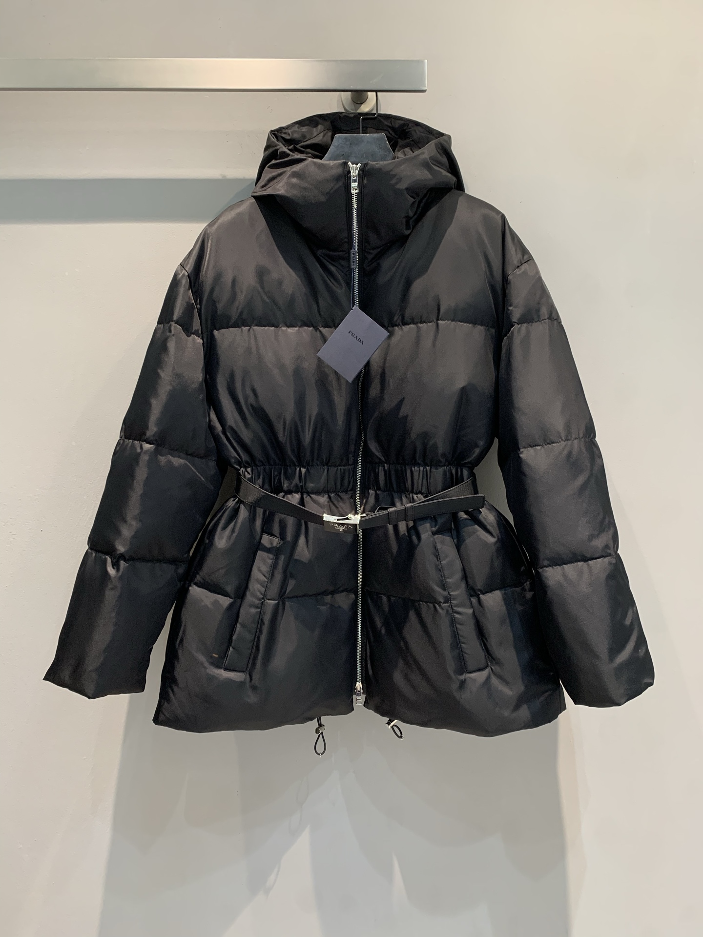 NO:544301,New model with dust bag shipped, real shot of large quantity  Prad*'s new autumn and winter fashionable and versatile belted hooded down jacket. The matte black nylon fabric is both textured and practical, and the national standard 90 white goose down has a full velvet layer to build a warm barrier; the hooded design protects the head and neck in winter, and the metal zipper runs neatly through the garment.  The body; the iconic belt girdles the exquisite waistline, the drawstring details at the hem hide ingenuity, and the dark gray brand tag highlights the high-end luxury status, making 'Prad*-style elegance' more eye-catching in the winter. Size SML, prada, down  jacket,hats,alexander wang19860909配防尘袋新款出货啦 大货实拍 Prad*秋冬新款时髦百搭束腰连帽羽绒服.哑光黑尼龙面料兼具质感与实穿,国标90白鹅绒饱满充绒层筑起温暖壁垒；连帽设计守护冬日头颈,金属拉链利落贯穿衣身；标志性腰带束出玲珑腰线,下摆抽绳细节暗藏巧思,深灰品牌吊牌彰显高奢身份,让“Prad*式优雅”在凛冬中愈发夺目.码数SML,,prada,down jacket,hats,alexander wang,Women's clothing