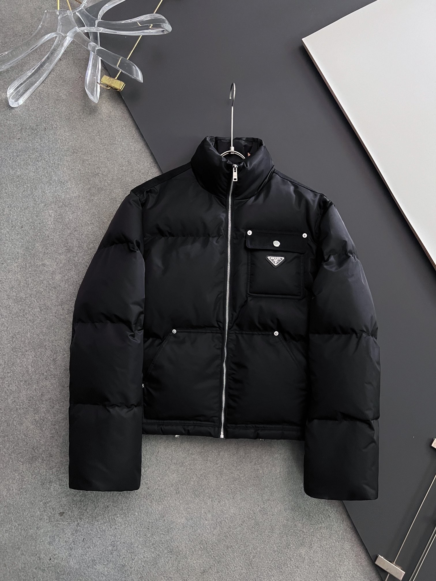 P495 Prad*2025春冬新款are-Nylon短款立领棉服夹克，这款Re-Nylon棉服夹克采用宽大廓形和运动风功能性设计。创新再生尼龙面料强化了现代实用主义特性，搭配温暖的填充，饰以涂珐琅三角形金属徽标，直筒衣袖拉链开合，Oversize版型
，上身效果非常帅气，强烈推荐！
码数:S M L XL