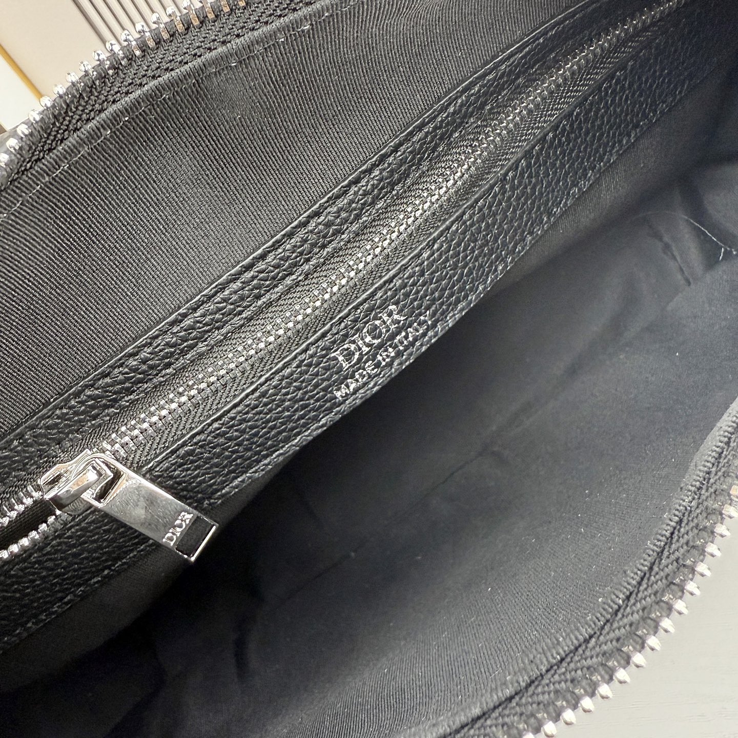 这款 Dior Slider 拉链水饺包是二零二五冬季男装系列新品，高雅时尚。廓形简约柔软，采用黑色 O