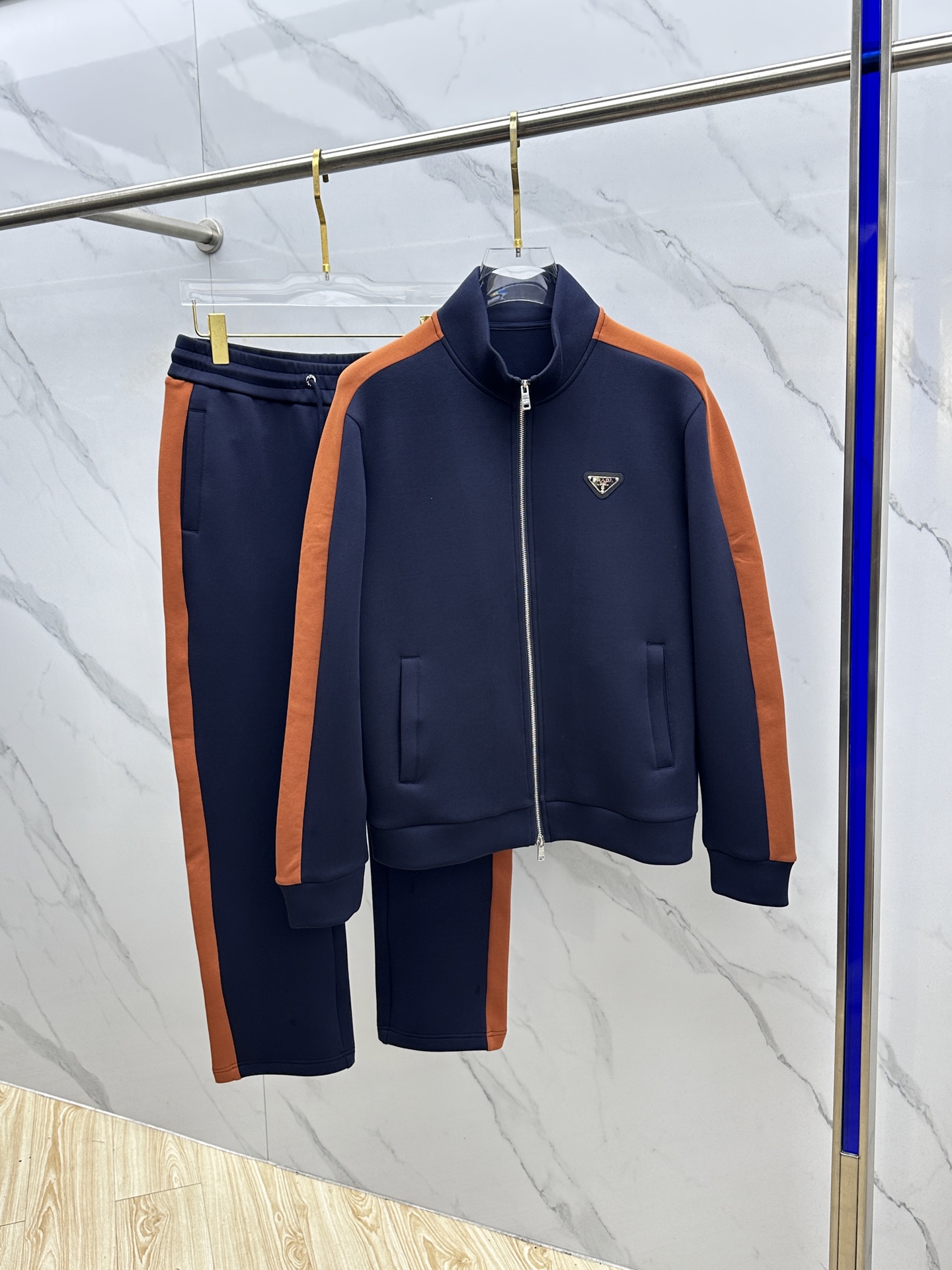 NO:527054,Prada 2025 Autumn and Winter Sports Series. High-density elastic fabrics build three-dimensional tailoring set, orange-brown stripes like track track tracks run through sleeves and trousers. The metal triangle logo shines brightly on the left chest and trousers side, injecting the precision craftsmanship of Milan Workshop into the sports genes. The aerospace-grade zipper system is as smooth as silk. The waist drawstring hides the PRADA relief head. The three-dimensional splicing ensures the ductility of the movement. From the morning run on Montenegro Street to the lunch of the Armani Hotel, the orange-brown stripes flow between the movements and become the coordinates of the movement. Hei Size M-3XL,,prada,prada,armani,alexander wang19860909Prada普拉达 2025秋冬运动系列.高密弹力面料构筑立体剪裁套装,橙棕条纹如赛道轨迹贯穿袖管与裤线.金属三角徽标在左胸与裤侧熠熠生辉,将米兰工坊的精密工艺注入运动基因. 航天级拉链系统顺滑如丝 裤腰抽绳暗藏PRADA浮雕字头 立体拼接确保运动延展性 从蒙特拿破仑大街的晨跑到阿玛尼酒店的午宴,橙棕条纹在动作间流转,成为移动的意式风格坐标.hei 尺码M-3XL,,prada,prada,armani,alexander wang,Men's clothing