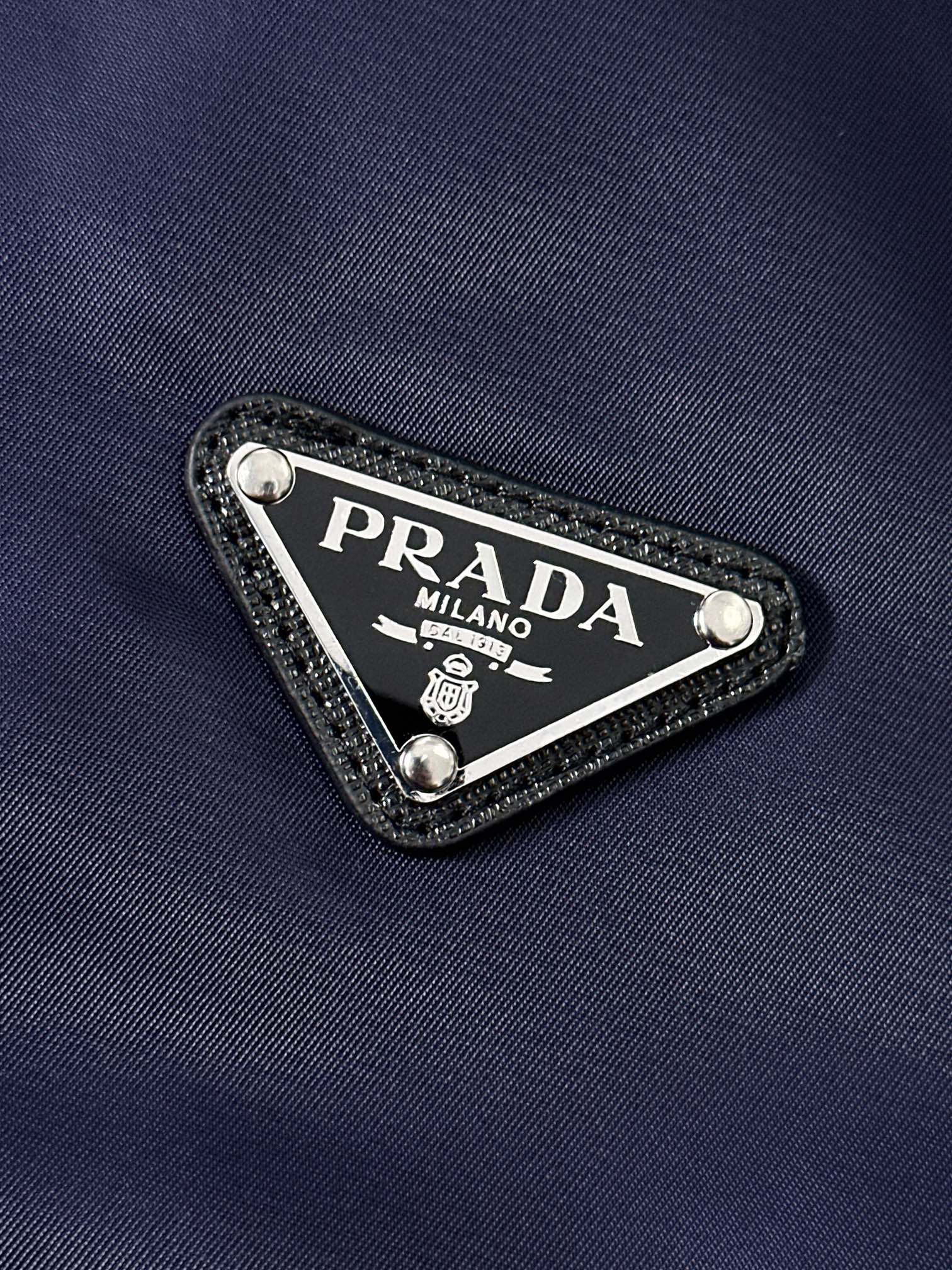 P320  891 PRA……普拉达 春秋季立领夹克！先上先卖，抢占先机。PRADA/普拉达 新品立领风衣外套。这款轻质尼龙夹克配有可拆卸帽和正面拉链，下摆特殊设计，颇具休闲装设计特色。胸前拼接口袋饰有标志性的三角形珐琅徽标，演绎品牌风范。正面拉链式口袋，饰有涂珐琅三角形金属徽标，正面拉链拉合，聚酰胺纤维面料。宝蓝 黑色 尺码：48-56