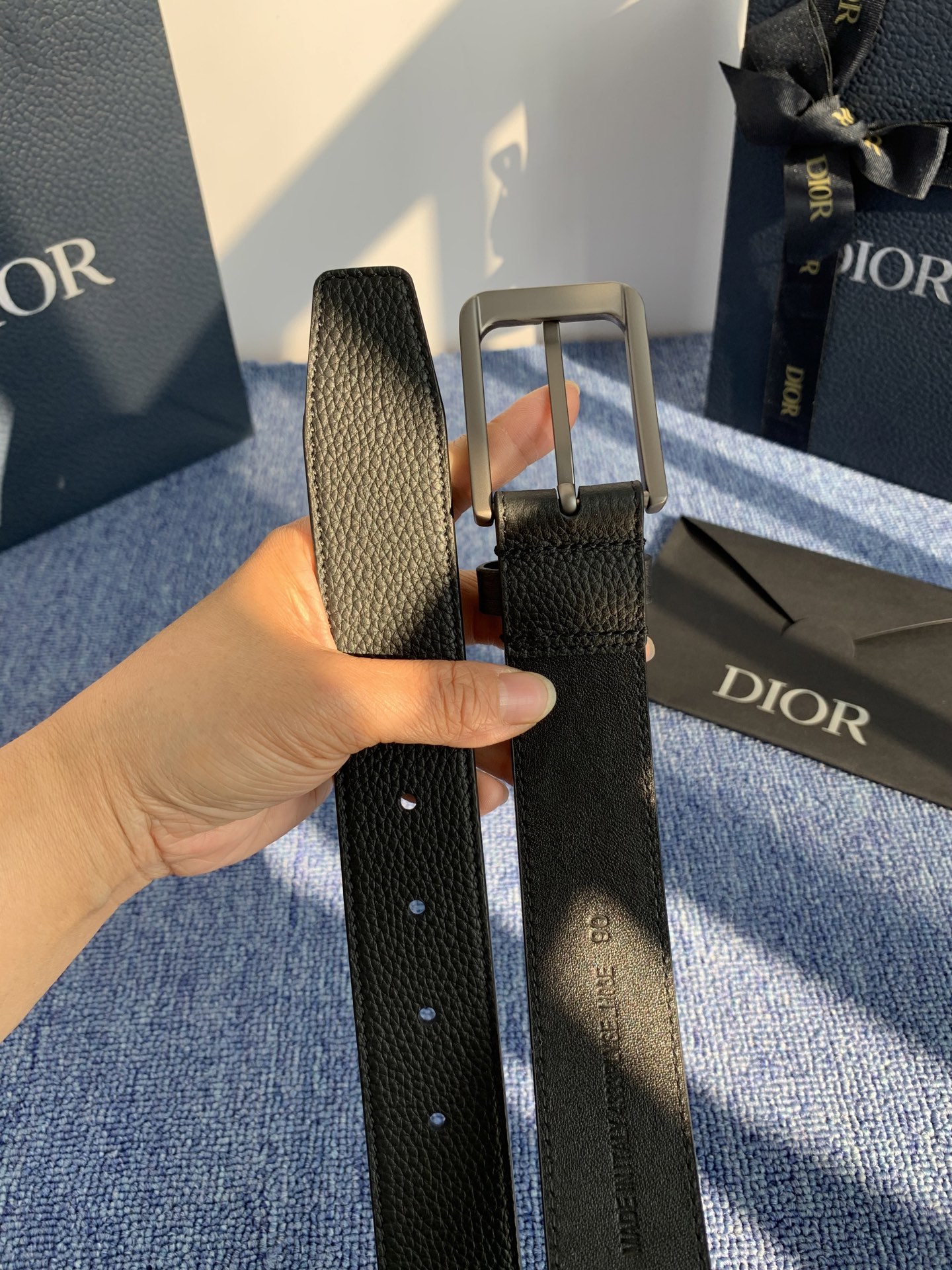 采用黑色粒面牛皮革精心制作，饰以镌刻有 Dior 的针扣和黑色金属覆层铜合金 CD Icon 标志腰带环