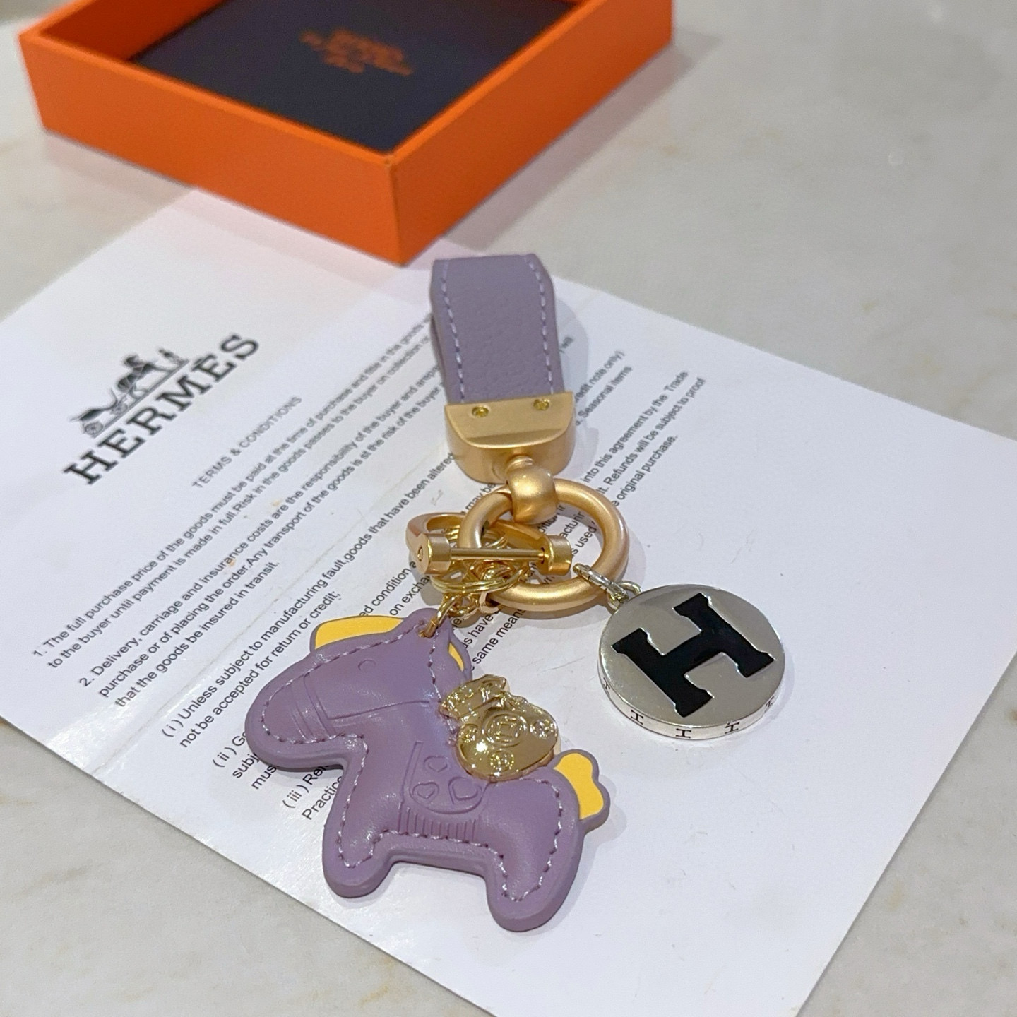 Hermes Rodeo Horse H Logo Key Charm pendant matte gold metal lavender purple leather silver-tone metal with black enamel H yellow leather accents 8cm total length