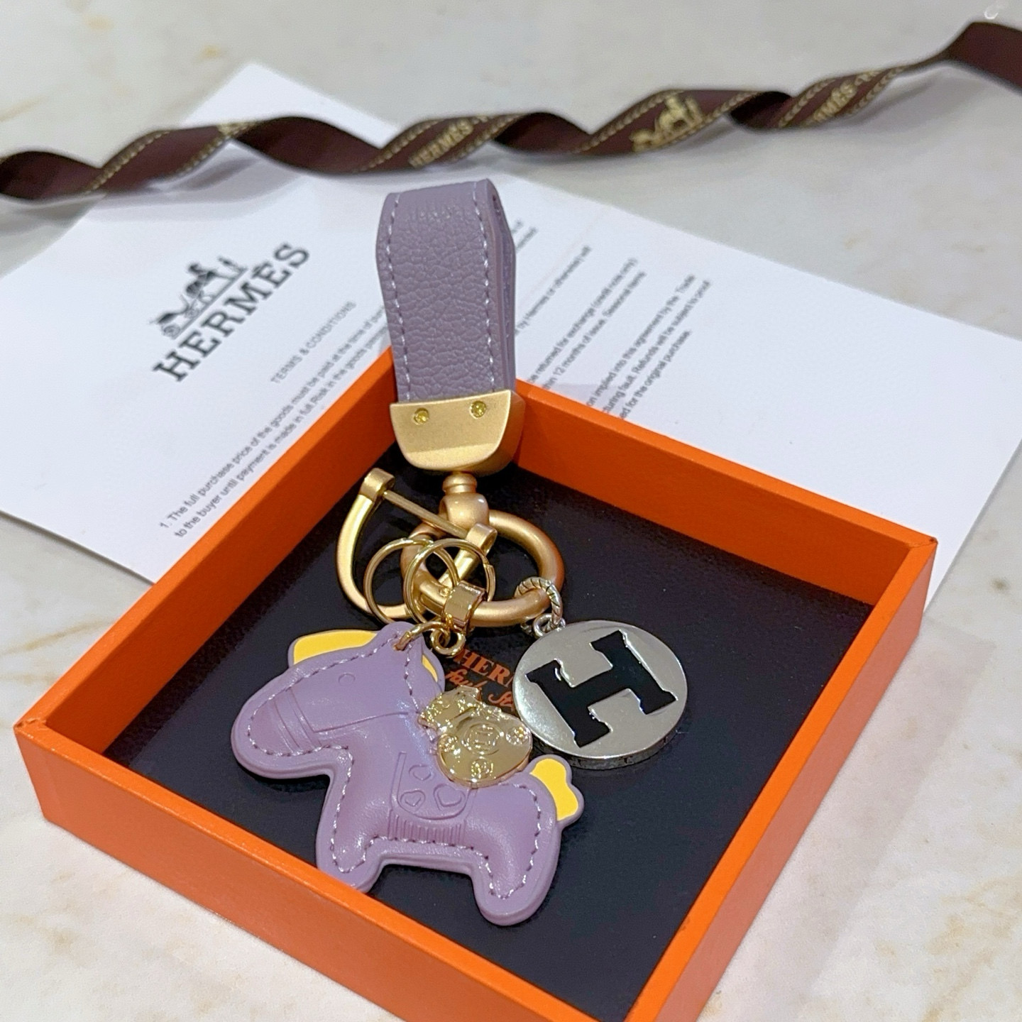 Hermes Rodeo Horse H Logo Key Charm pendant matte gold metal lavender purple leather silver-tone metal with black enamel H yellow leather accents 8cm total length