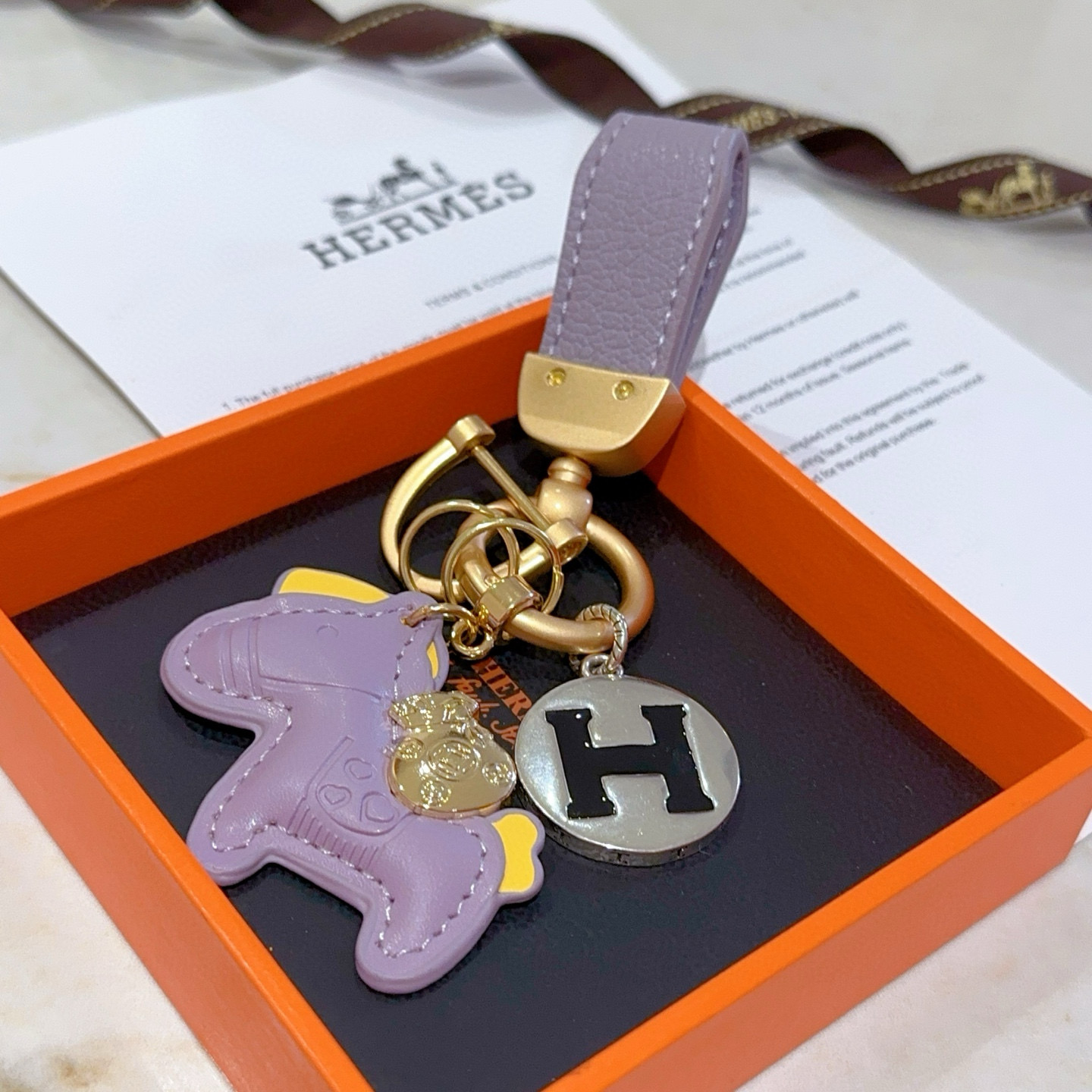 Hermes Rodeo Horse H Logo Key Charm pendant matte gold metal lavender purple leather silver-tone metal with black enamel H yellow leather accents 8cm total length