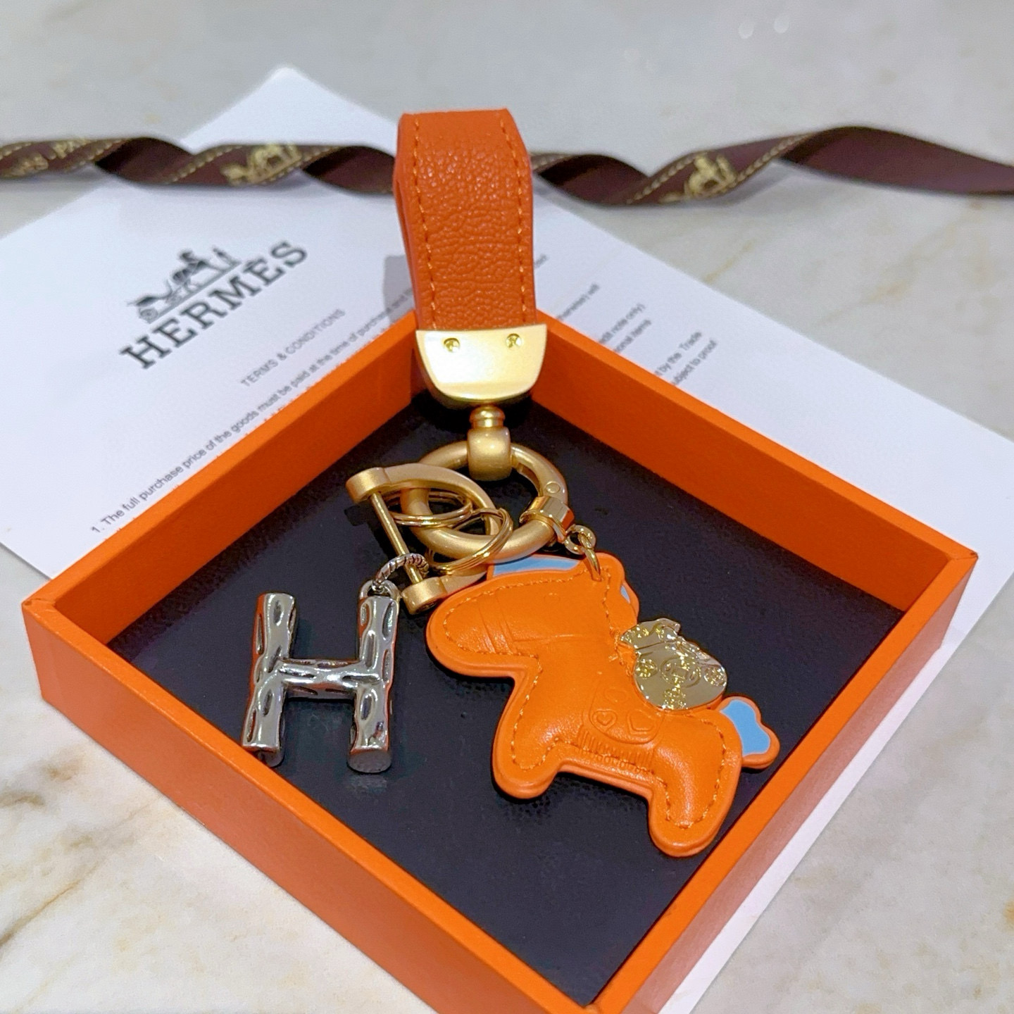 Pendentif Hermes Rodeo Pegase H Logo Key Charm Cuir orange avec accents bleu clair Quincaillerie en métal doré et argenté Longueur totale 8 cm