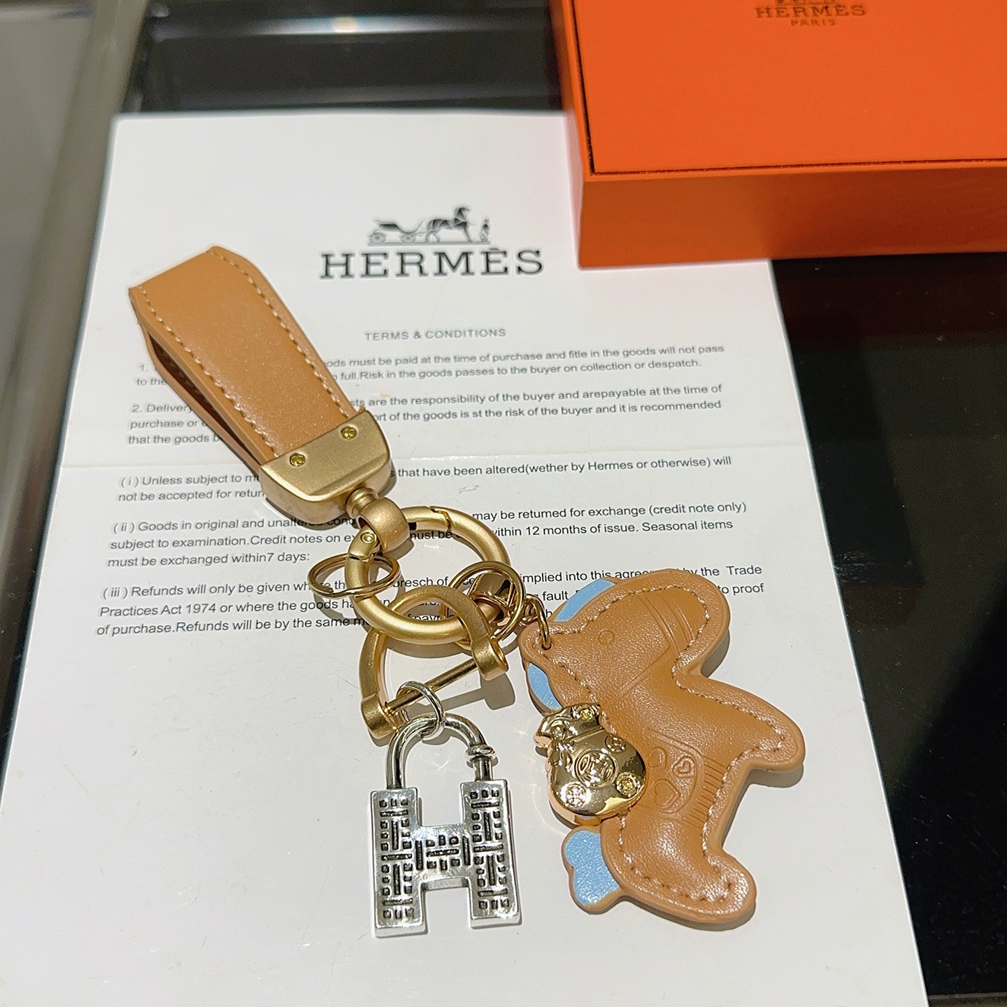 Chaveiro com pingente de cavalo Hermes, couro bronzeado com detalhes em azul claro, hardware dourado fosco, tom prateado, pingente H, comprimento total de 10 cm