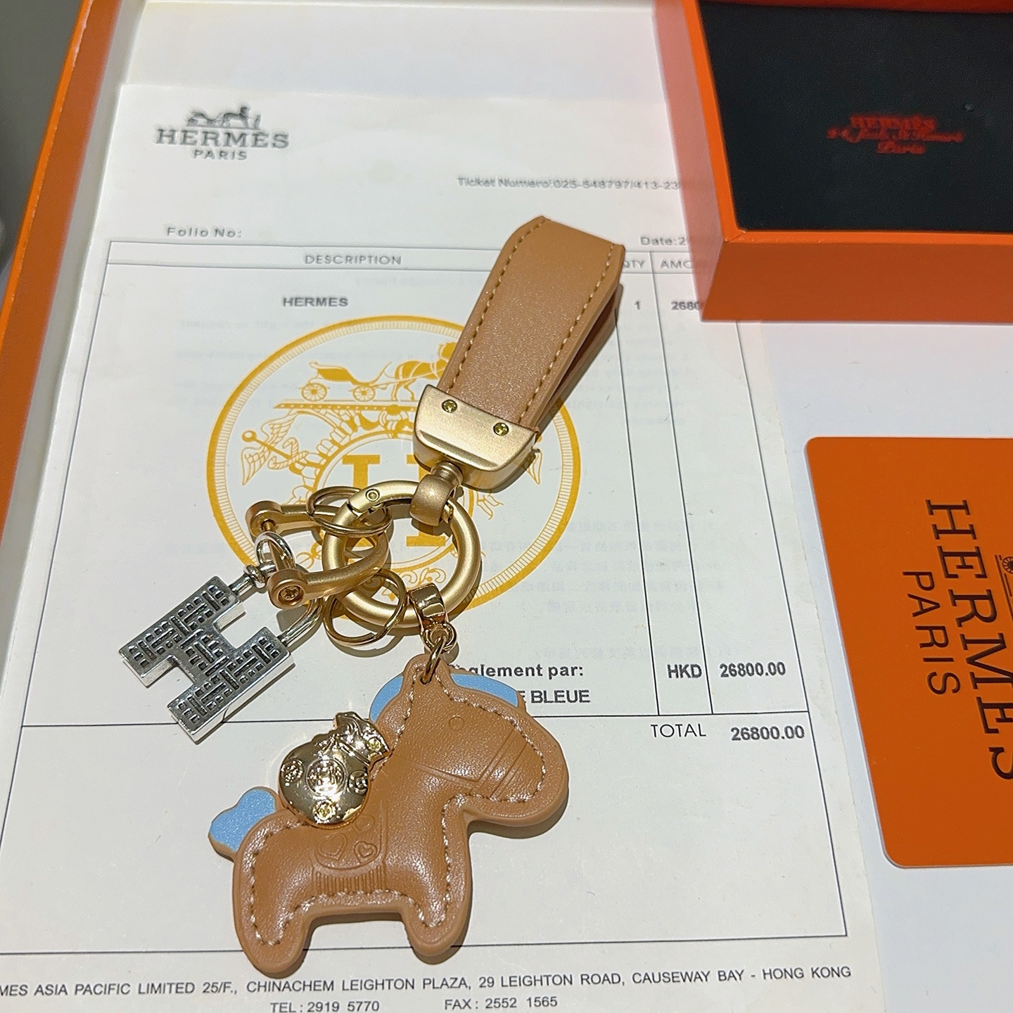 Chaveiro com pingente de cavalo Hermes, couro bronzeado com detalhes em azul claro, hardware dourado fosco, tom prateado, pingente H, comprimento total de 10 cm