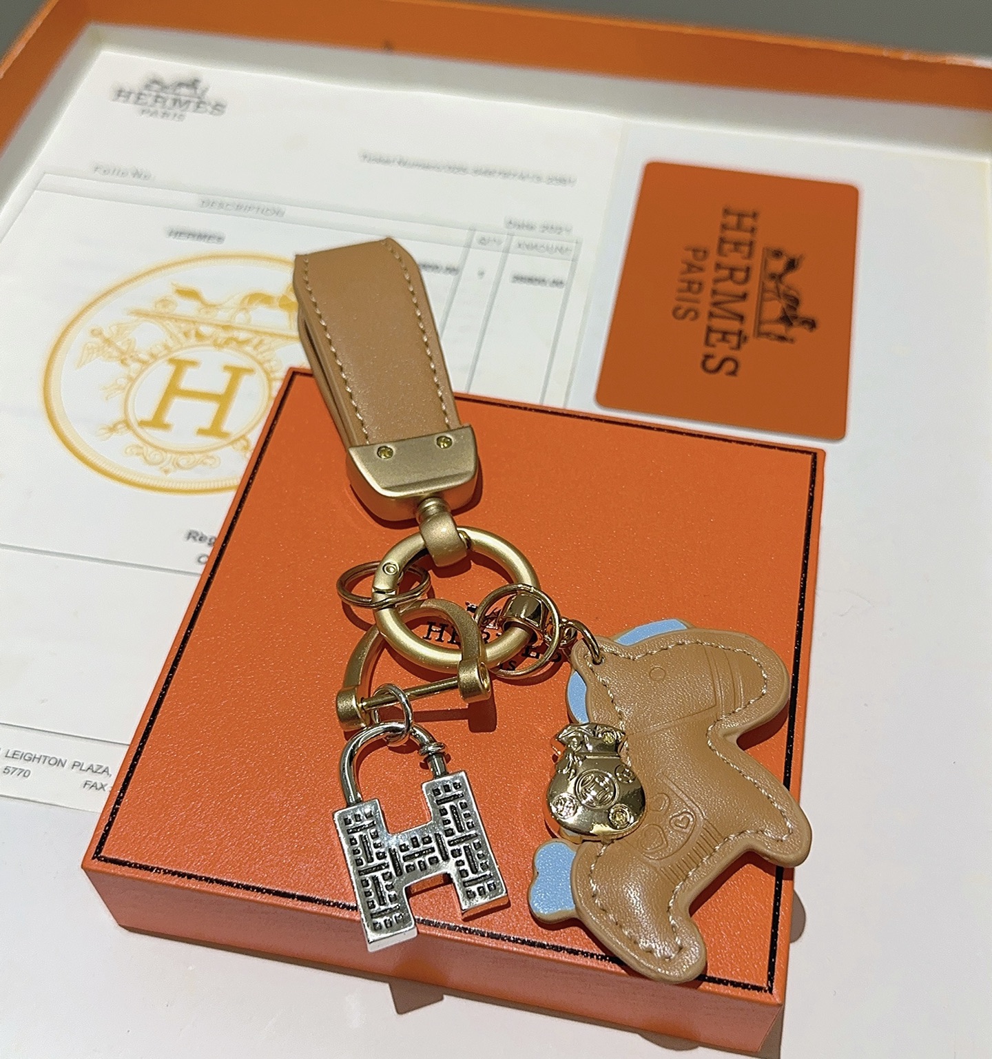 Chaveiro com pingente de cavalo Hermes, couro bronzeado com detalhes em azul claro, hardware dourado fosco, tom prateado, pingente H, comprimento total de 10 cm