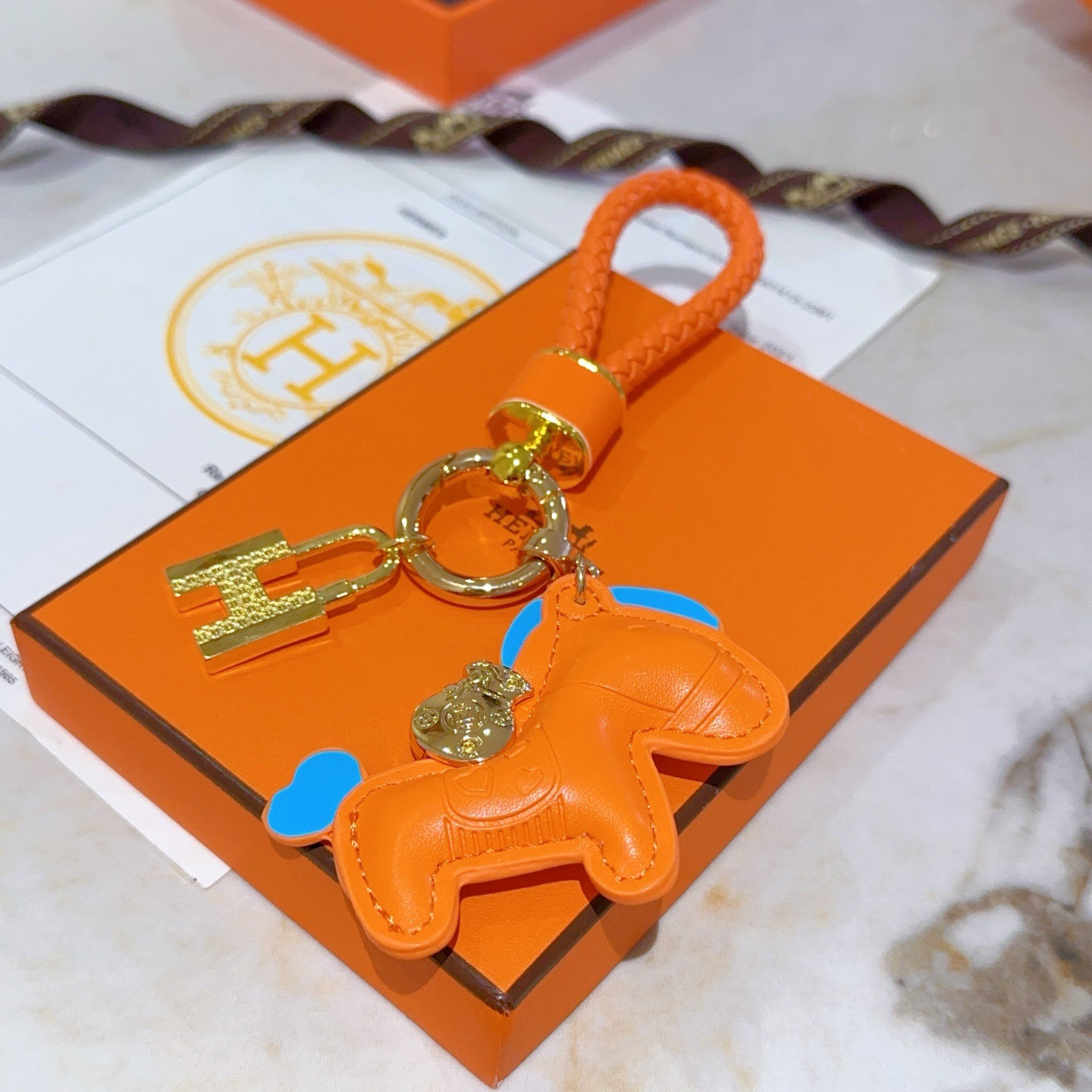 Ciondolo Hermes Rodeo H Lock Key Charm Ciondolo cavallo in pelle arancione intrecciata in pelle intrecciata arancione in metallo color oro con accenti blu, lunghezza totale 10 cm