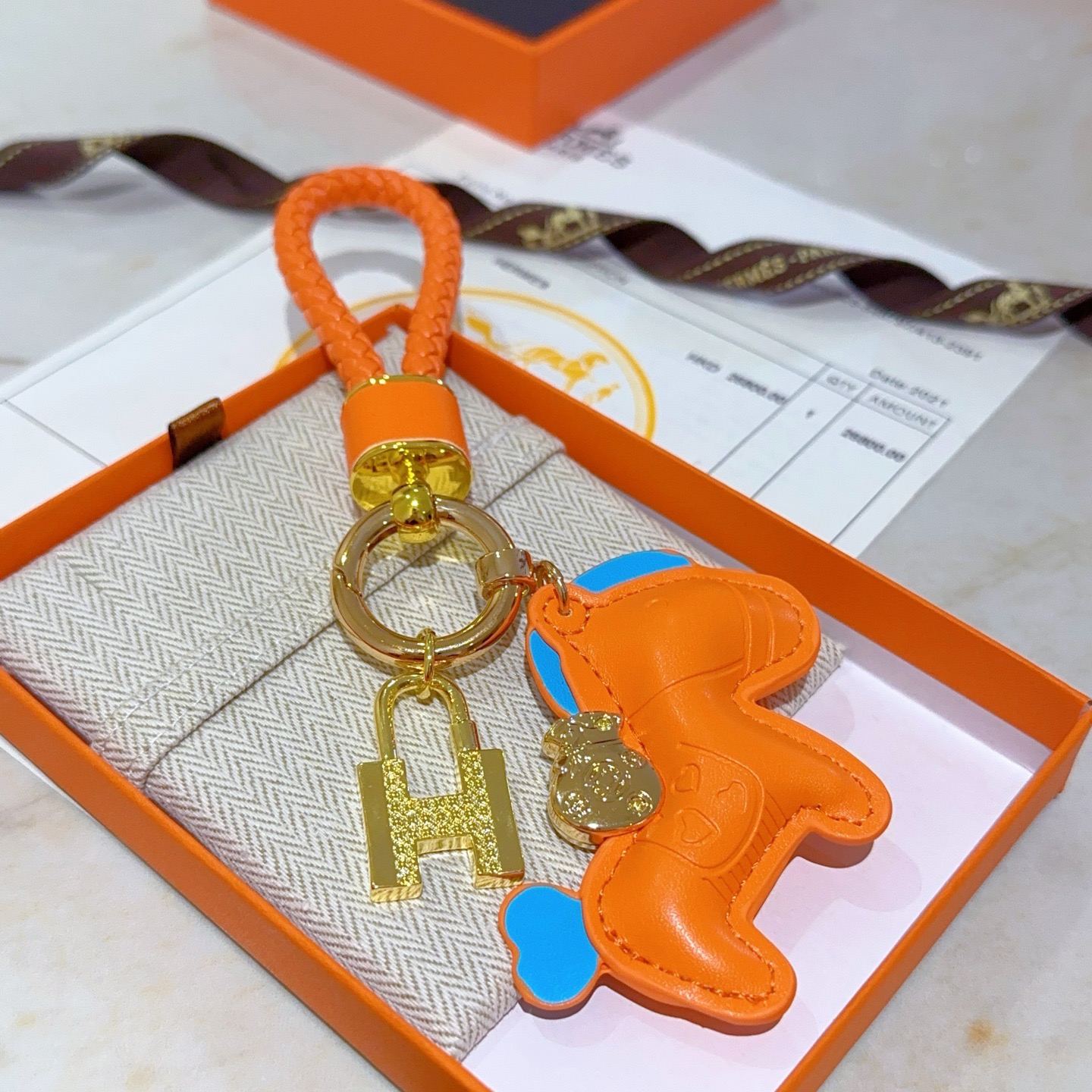Ciondolo Hermes Rodeo H Lock Key Charm Ciondolo cavallo in pelle arancione intrecciata in pelle intrecciata arancione in metallo color oro con accenti blu, lunghezza totale 10 cm