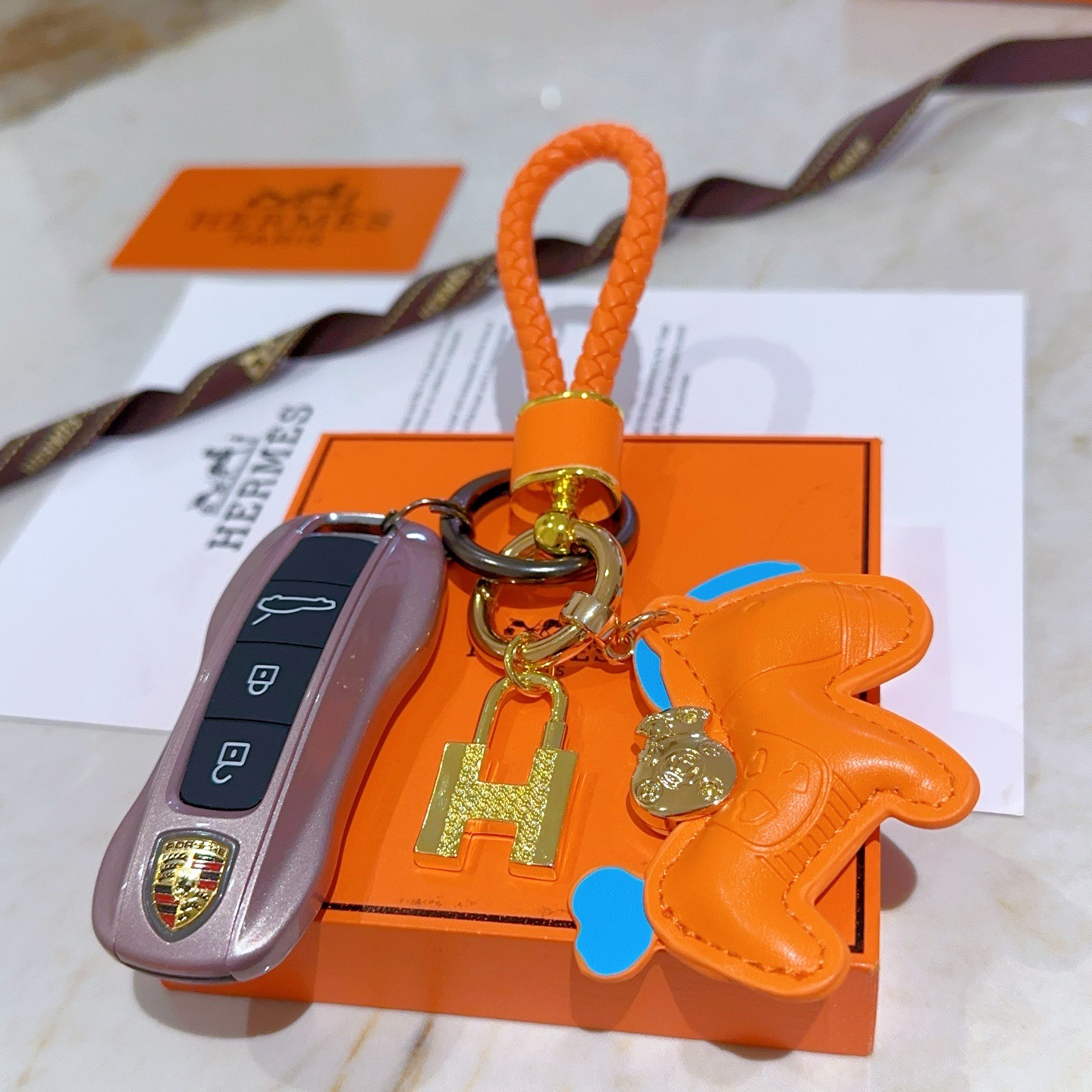 Ciondolo Hermes Rodeo H Lock Key Charm Ciondolo cavallo in pelle arancione intrecciata in pelle intrecciata arancione in metallo color oro con accenti blu, lunghezza totale 10 cm