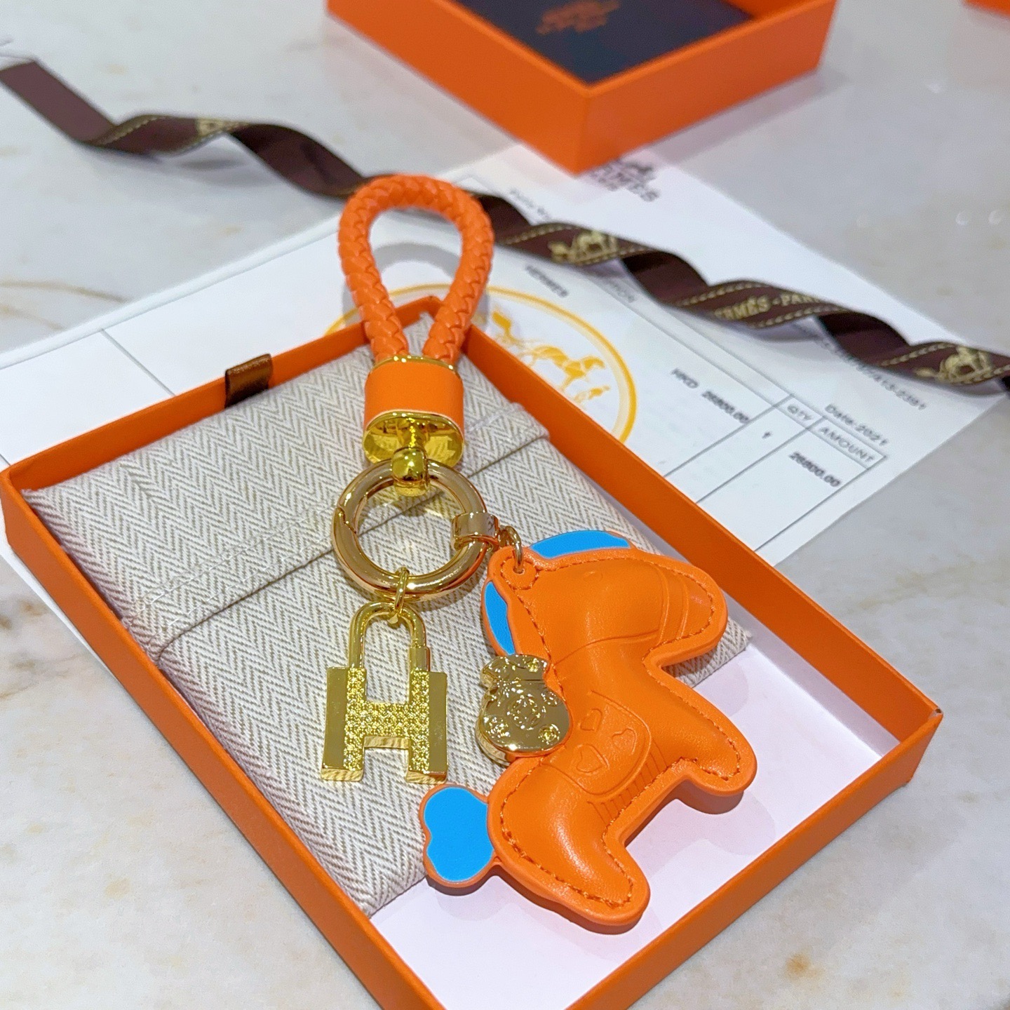Ciondolo Hermes Rodeo H Lock Key Charm Ciondolo cavallo in pelle arancione intrecciata in pelle intrecciata arancione in metallo color oro con accenti blu, lunghezza totale 10 cm