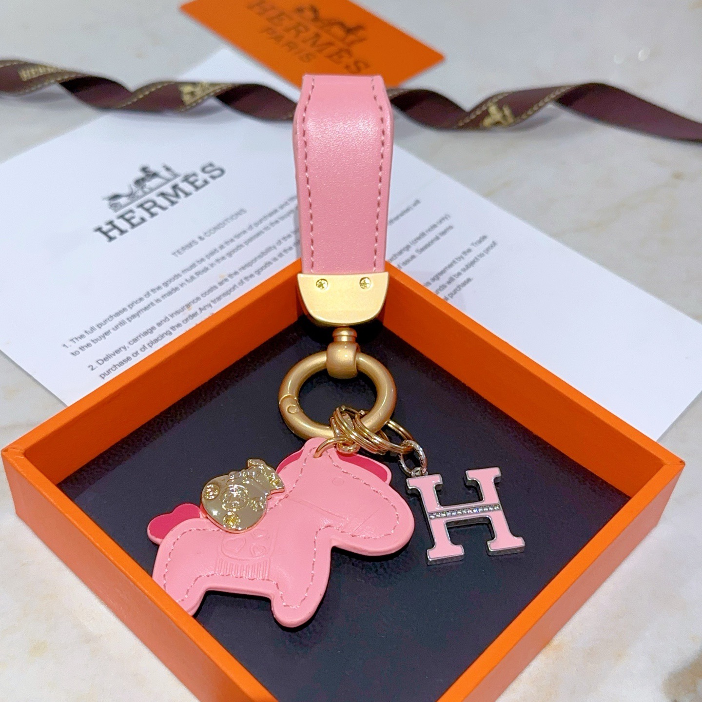 Chaveiro com logotipo Hermes Rodeo H Pingente de couro rosa com metal dourado esmalte rosa Pingente H com detalhes em cristal transparente 10 cm de comprimento total