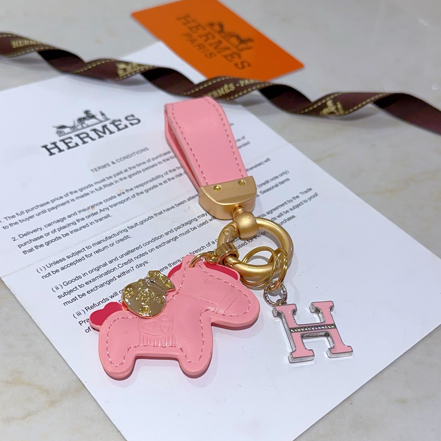 Chaveiro com logotipo Hermes Rodeo H Pingente de couro rosa com metal dourado esmalte rosa Pingente H com detalhes em cristal transparente 10 cm de comprimento total