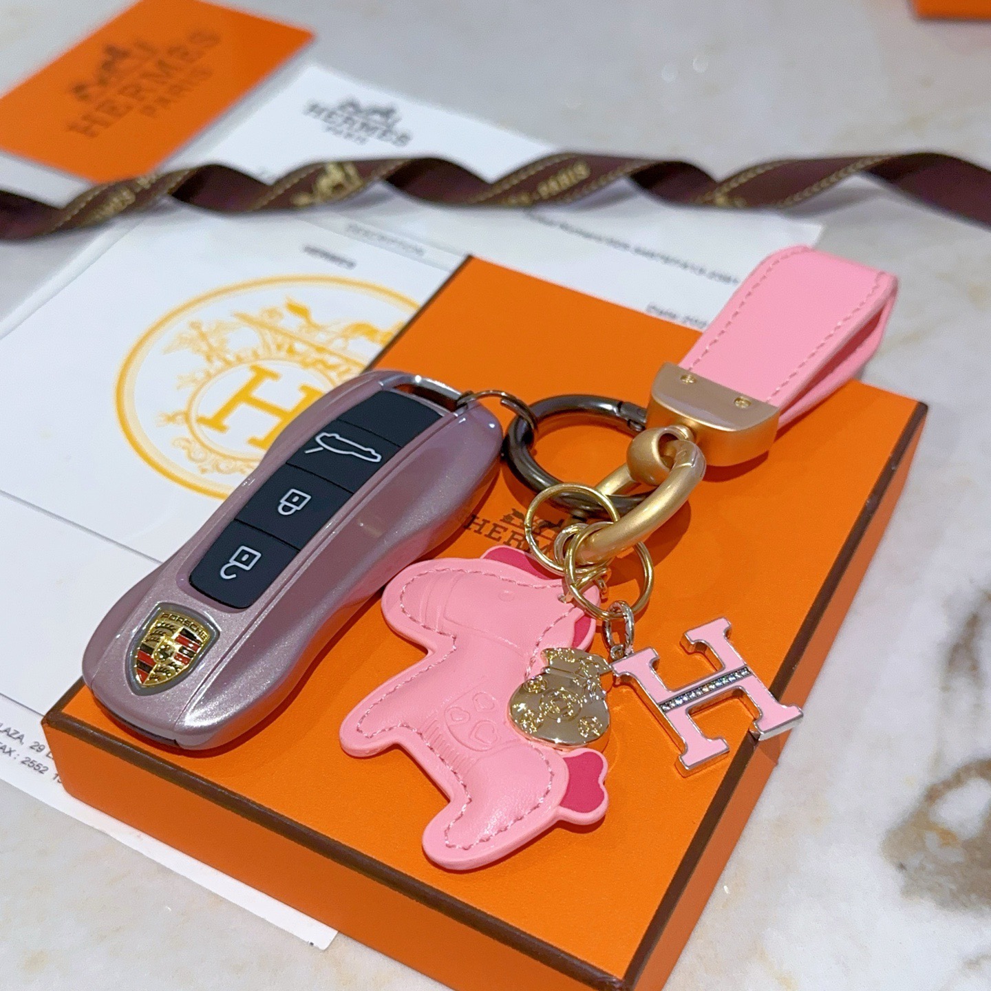 Chaveiro com logotipo Hermes Rodeo H Pingente de couro rosa com metal dourado esmalte rosa Pingente H com detalhes em cristal transparente 10 cm de comprimento total
