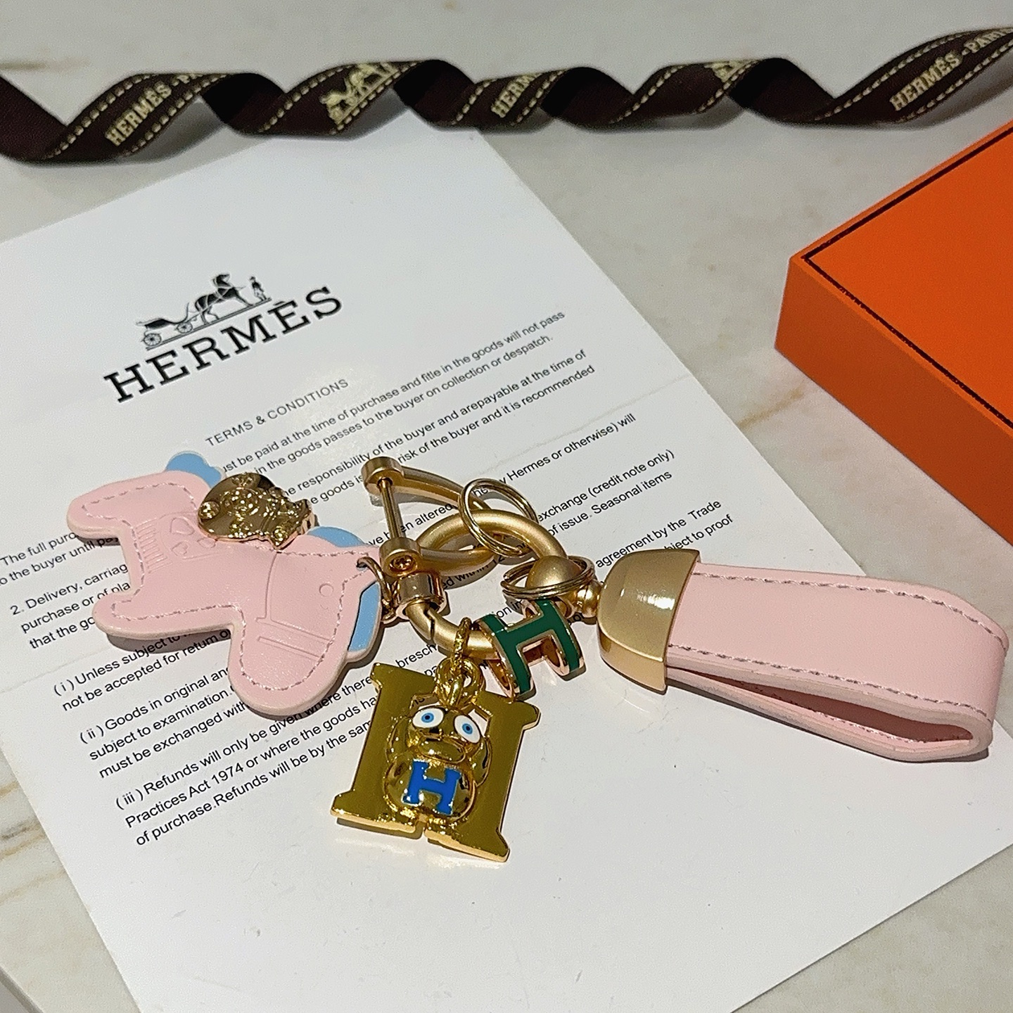 Hermes Rodeo H Logo Cartoon Charm Chaveiro pingente Couro rosa com detalhes em azul claro metal dourado detalhes em esmalte verde e azul 10 cm de comprimento total