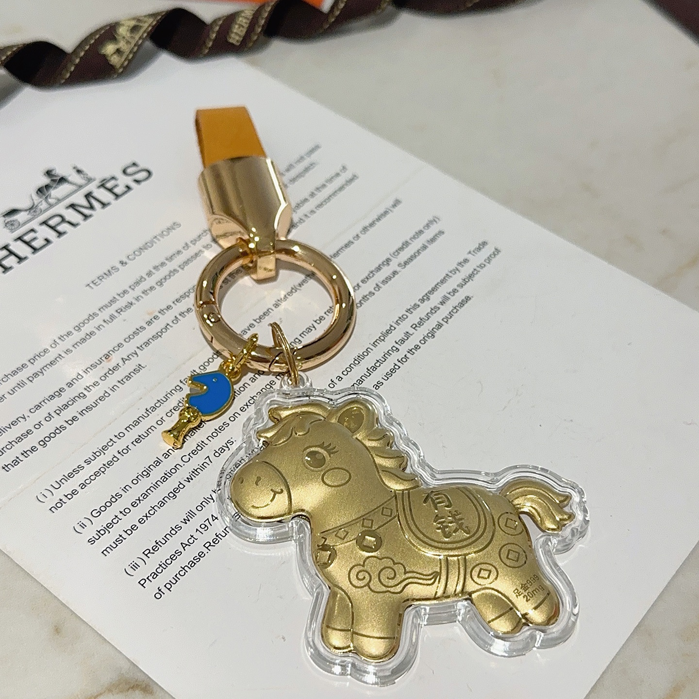 Hermes Lucky Horse Charm Keychain pendant Gold-tone metal with orange leather strap blue enamel accent clear protective casing over gold horse charm Total length 9cm