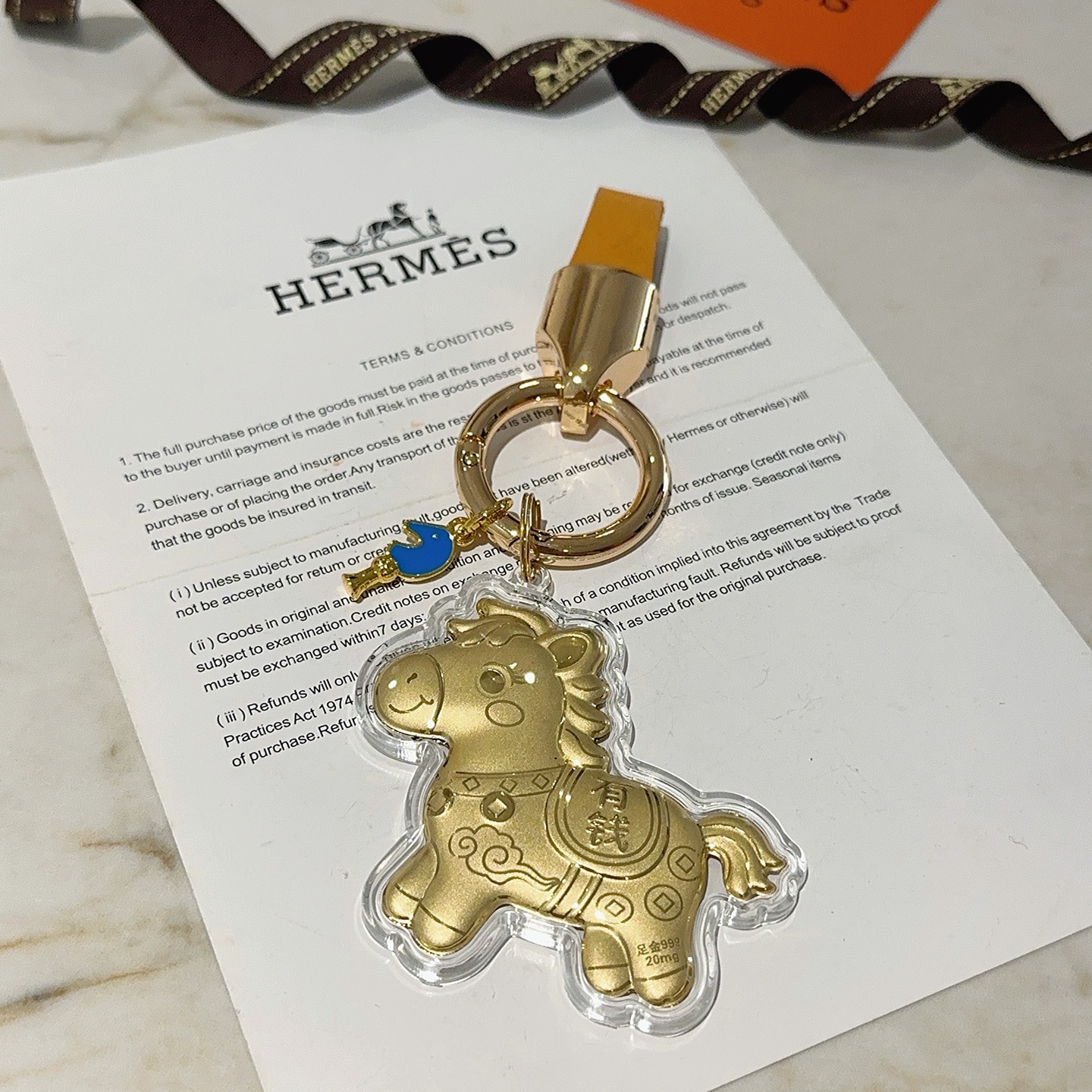 Hermes Lucky Horse Charm Keychain pendant Gold-tone metal with orange leather strap blue enamel accent clear protective casing over gold horse charm Total length 9cm