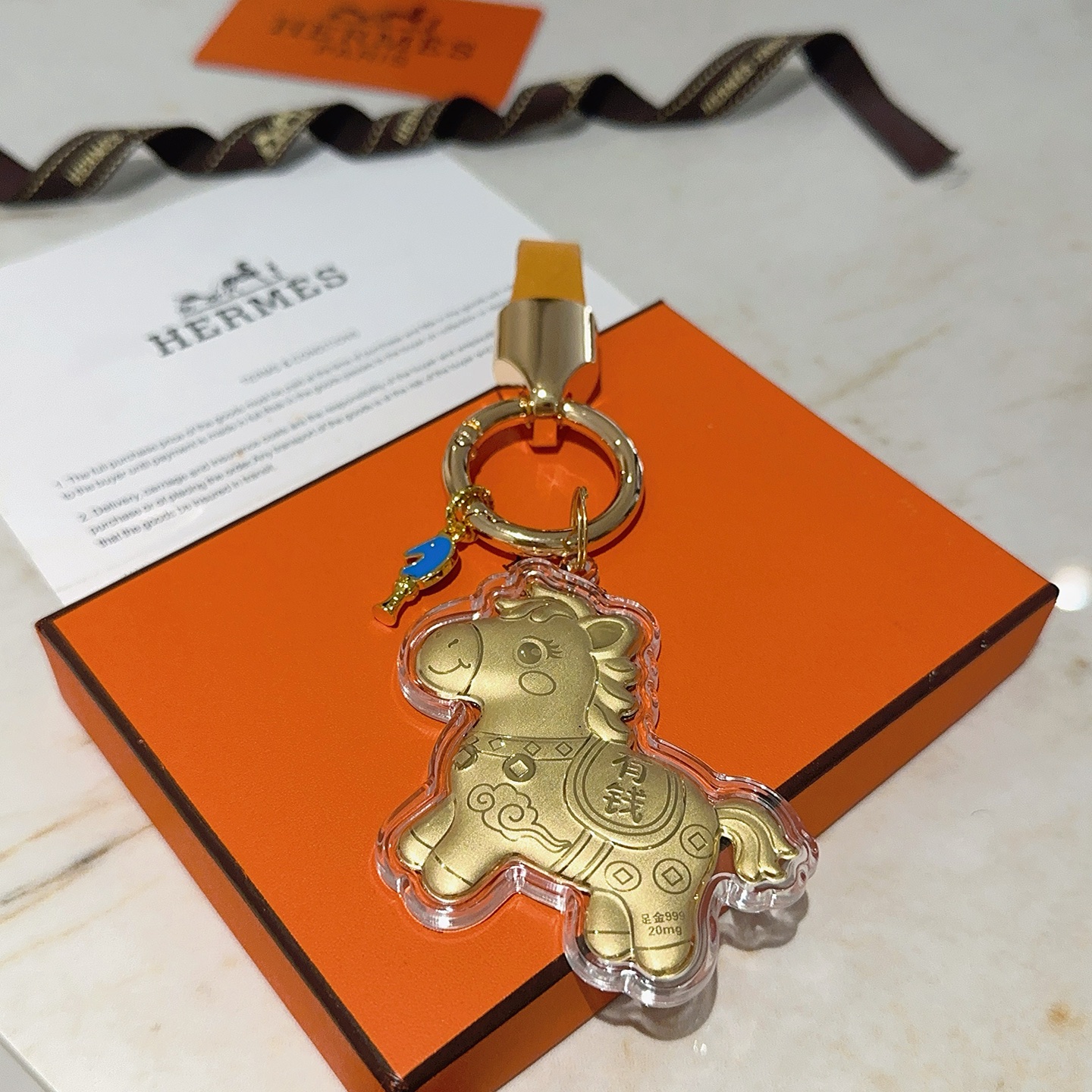 Hermes Lucky Horse Charm Keychain pendant Gold-tone metal with orange leather strap blue enamel accent clear protective casing over gold horse charm Total length 9cm