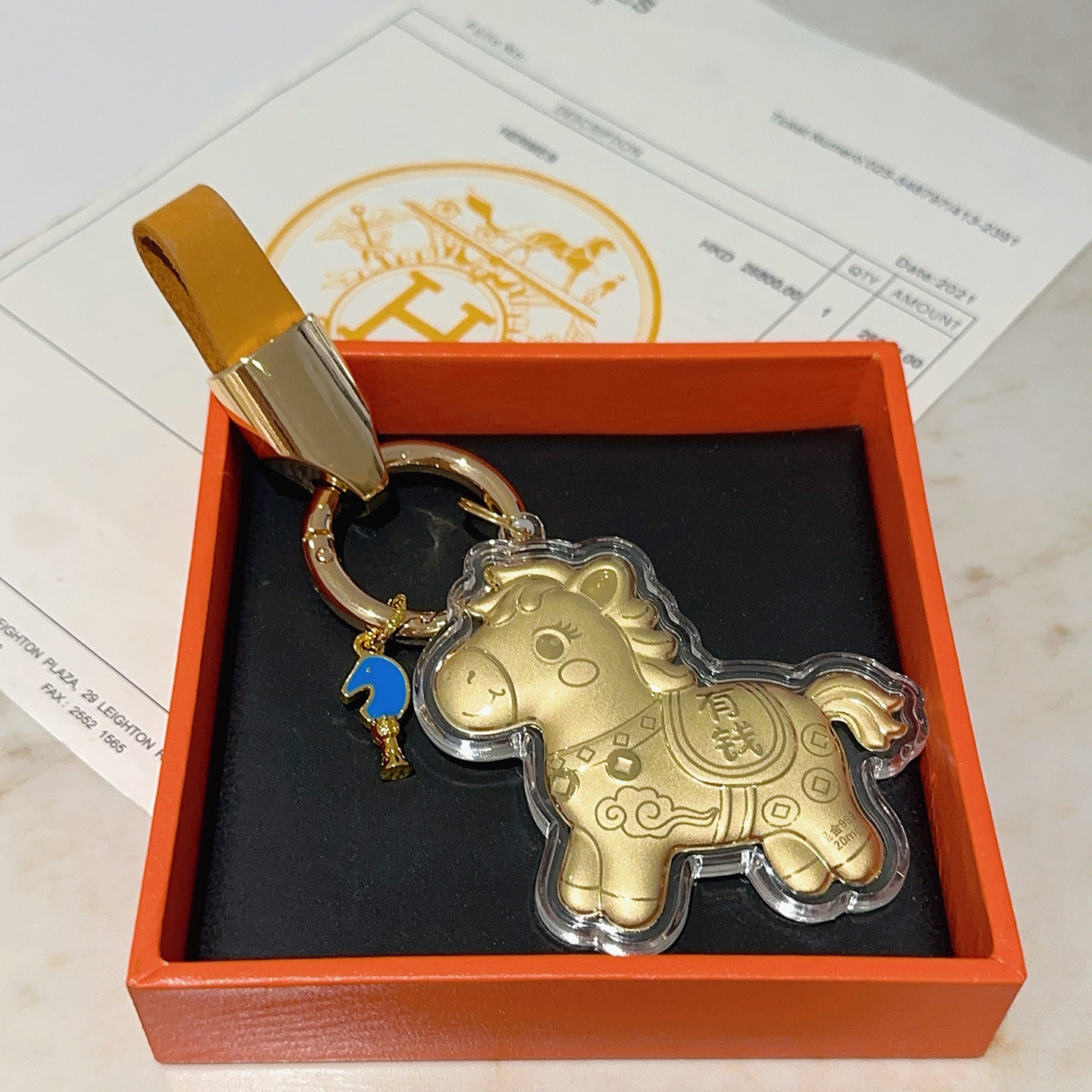Hermes Lucky Horse Charm Keychain pendant Gold-tone metal with orange leather strap blue enamel accent clear protective casing over gold horse charm Total length 9cm