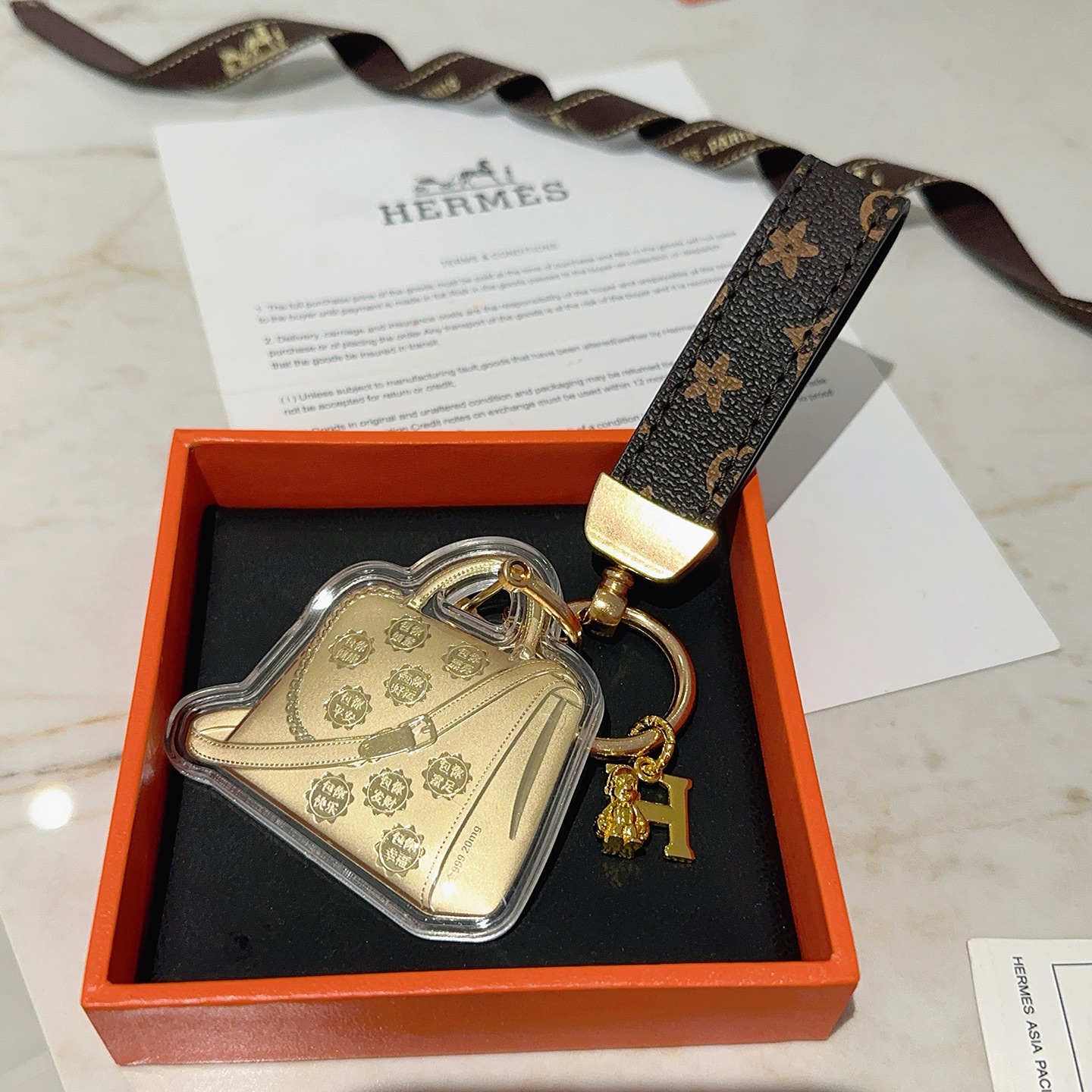 Hermes Bolide Bag Charm Porte-clés pendentif Métal doré monogramme marron foncé toile enduite boîtier en acrylique transparent longueur totale 12 cm