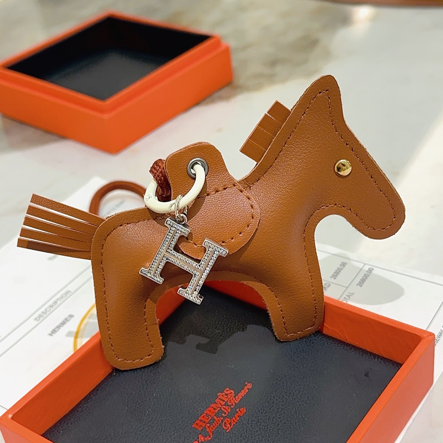 Hermes Rodeo Pegase Horse Bag Charm with H Pendant pendant Gold brown leather silver-tone metal with clear crystal pave H charm gold-tone metal rivet off-white hardware brown woven cord strap 10cm total charm length 8cm