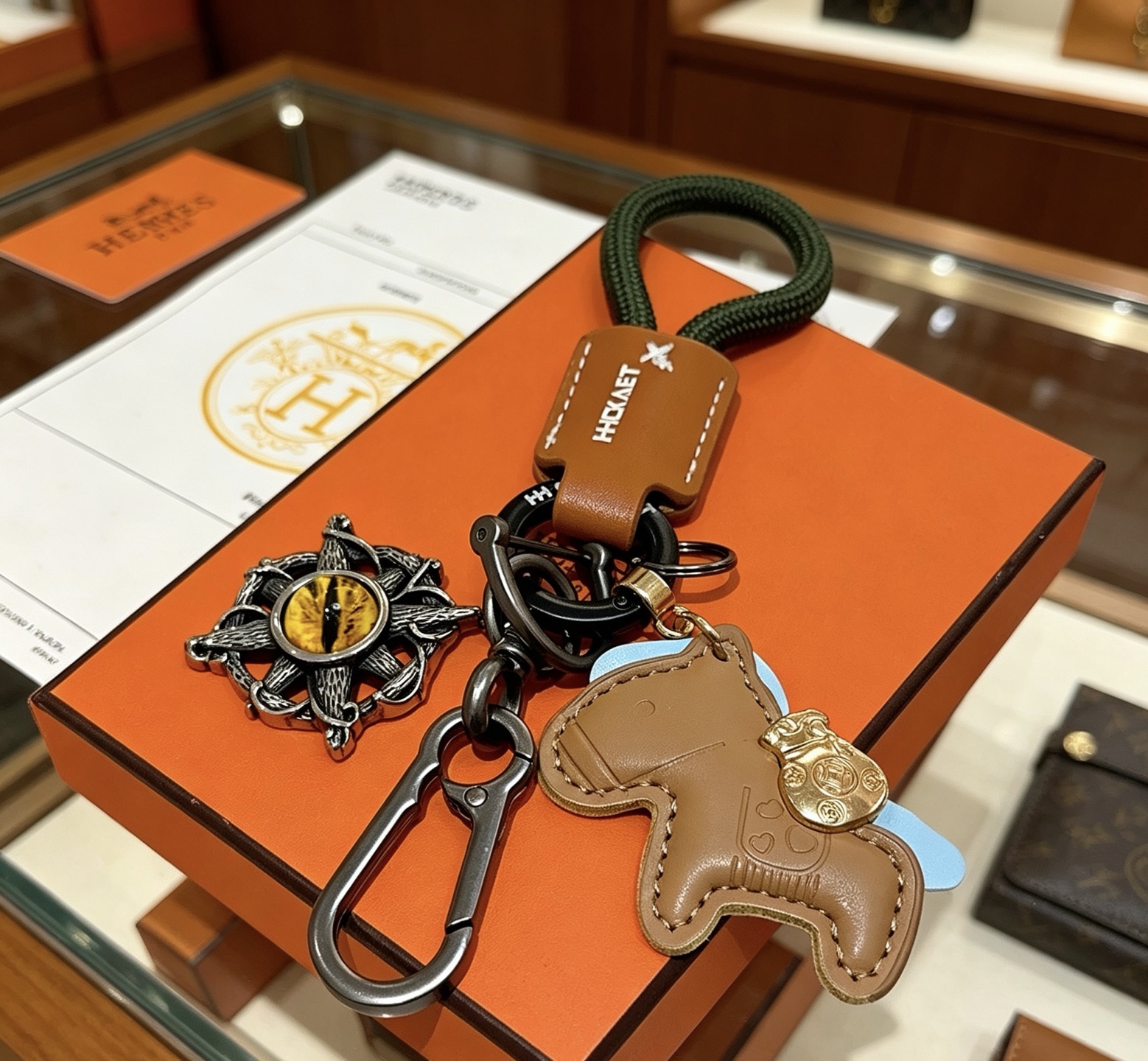 Hermes Rodeo Horse Charm Portachiavi Ciondolo in pelle marrone chiaro Cavo intrecciato verde scuro Hardware in canna di fucile Accento in metallo color oro Pietra gialla occhio di gatto Supporto azzurro 10 cm Lunghezza totale