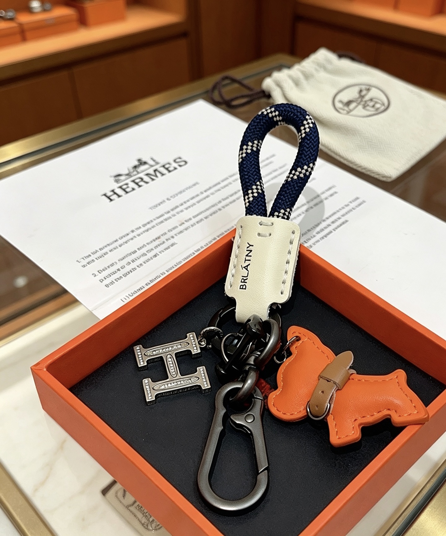 Hermes BRLATNY Puppy H Charm Keychain pendant Gunmetal black hardware orange leather puppy charm off-white leather tag navy blue with white woven rope brown leather collar detail 12cm total length