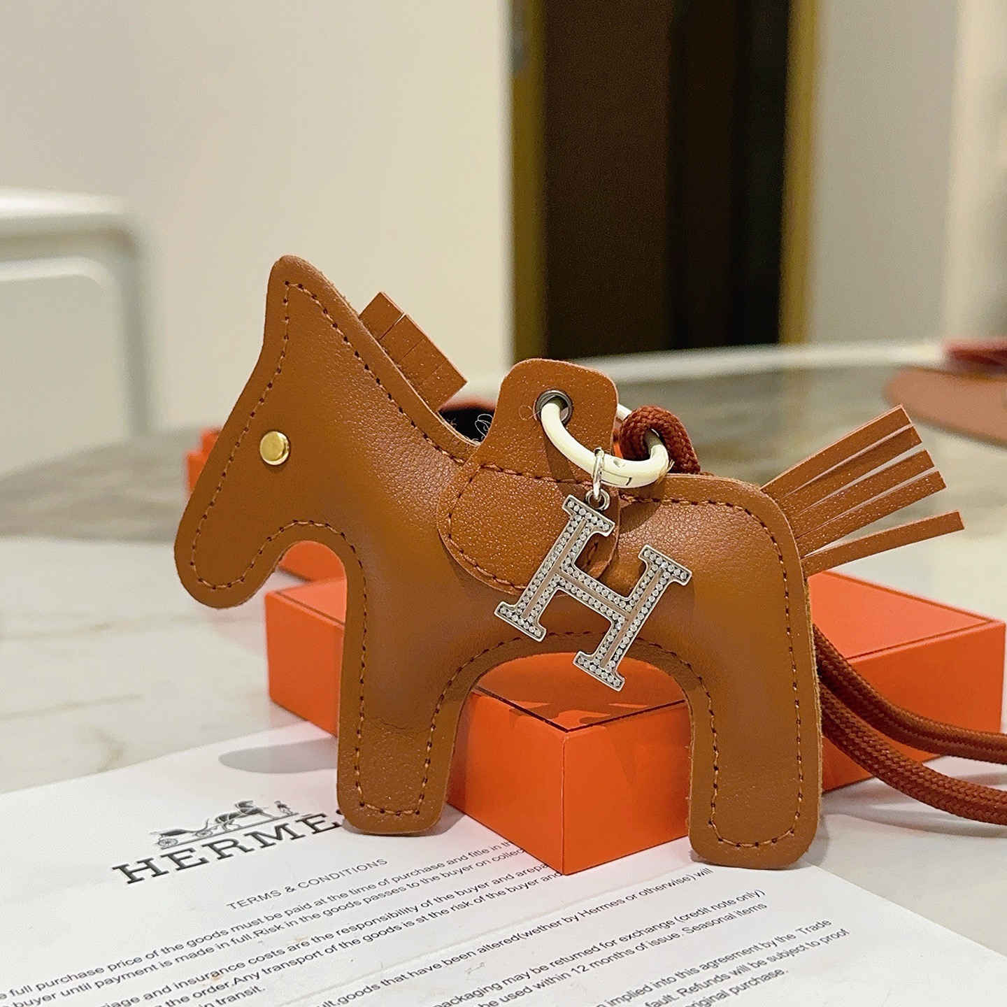 Breloque de sac à cheval Hermes Rodeo Pegase avec pendentif en cristal H Pendentif Cuir marron doré Métal argenté avec pavé de cristaux transparents Quincaillerie blanc cassé Cordon marron terre cuite Longueur totale de la breloque 12 cm Bracelet de cordon de 8 cm