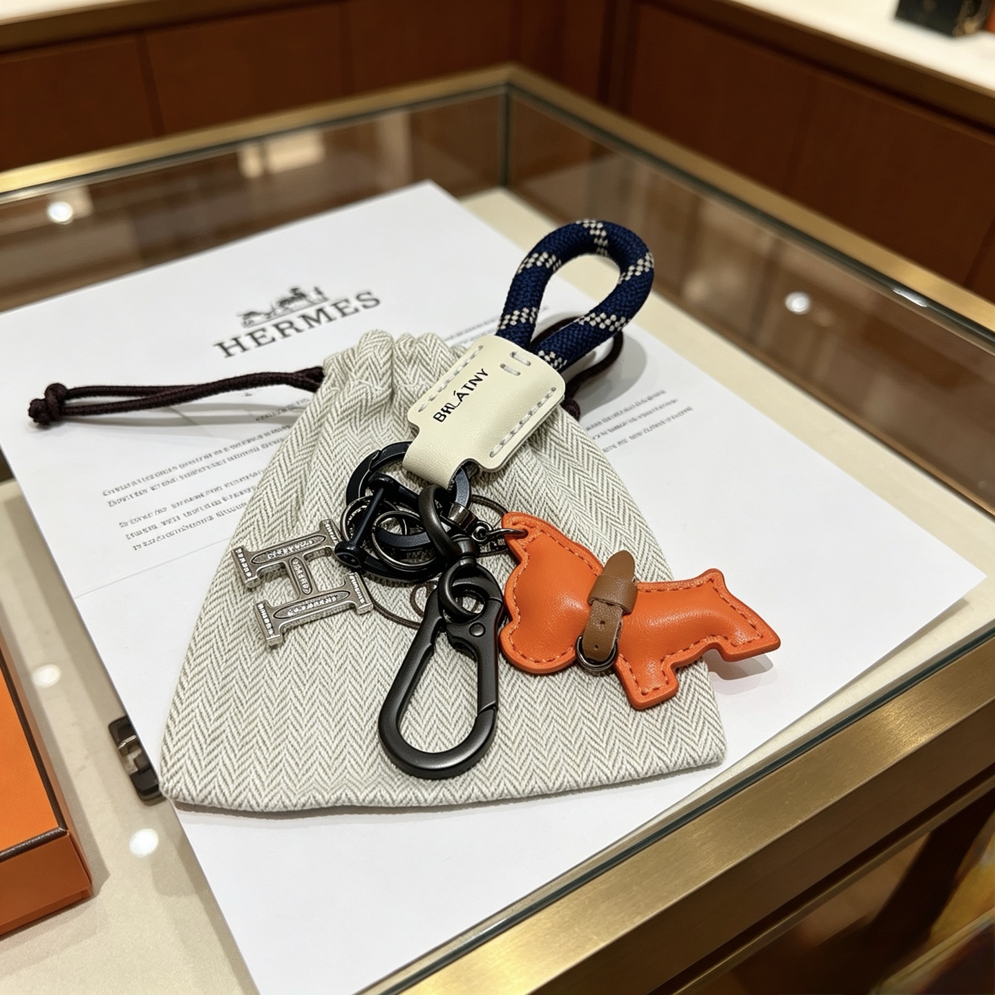 Hermes BRLATNY Puppy H Charm Keychain pendant Gunmetal hardware navy blue with white check woven strap off-white leather tag orange leather puppy charm with brown leather collar clear crystal accents on H charm 10cm total length