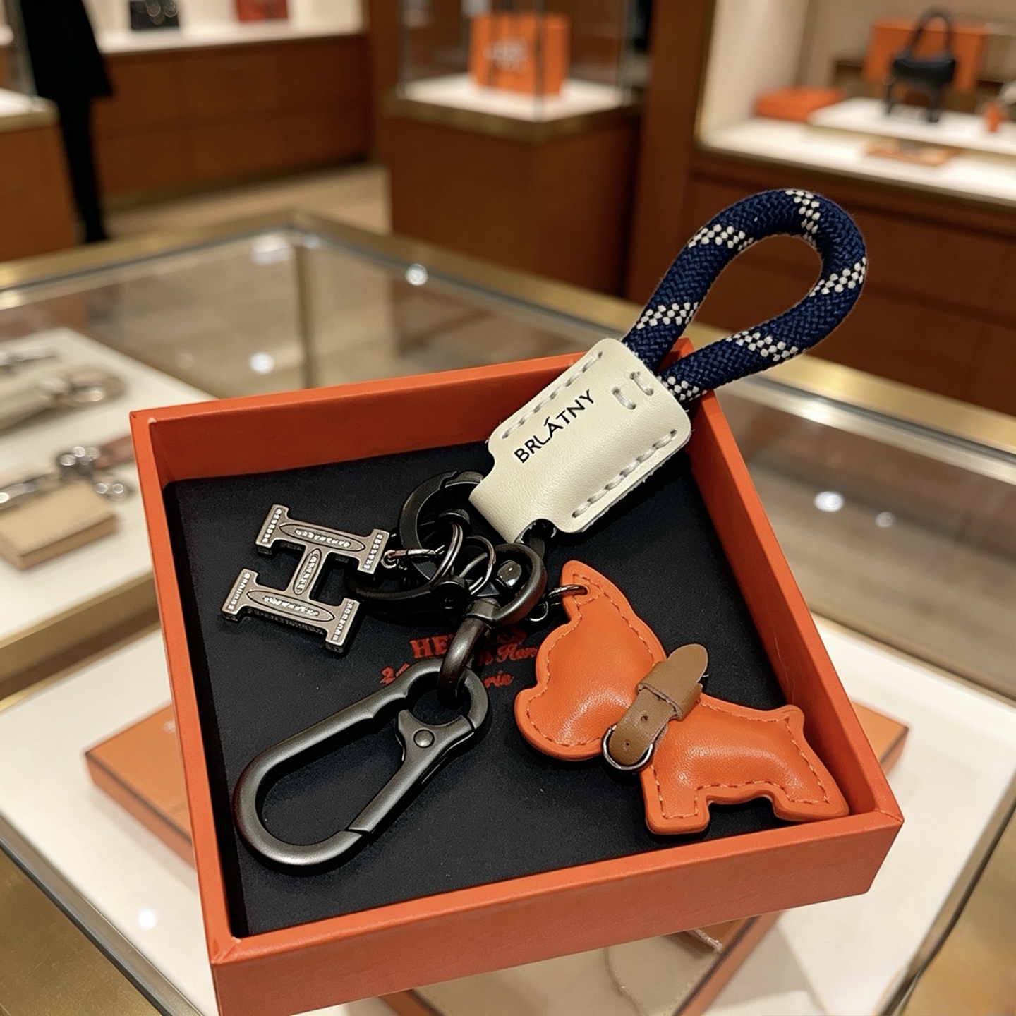 Hermes BRLATNY Puppy H Charm Keychain pendant Gunmetal hardware navy blue with white check woven strap off-white leather tag orange leather puppy charm with brown leather collar clear crystal accents on H charm 10cm total length