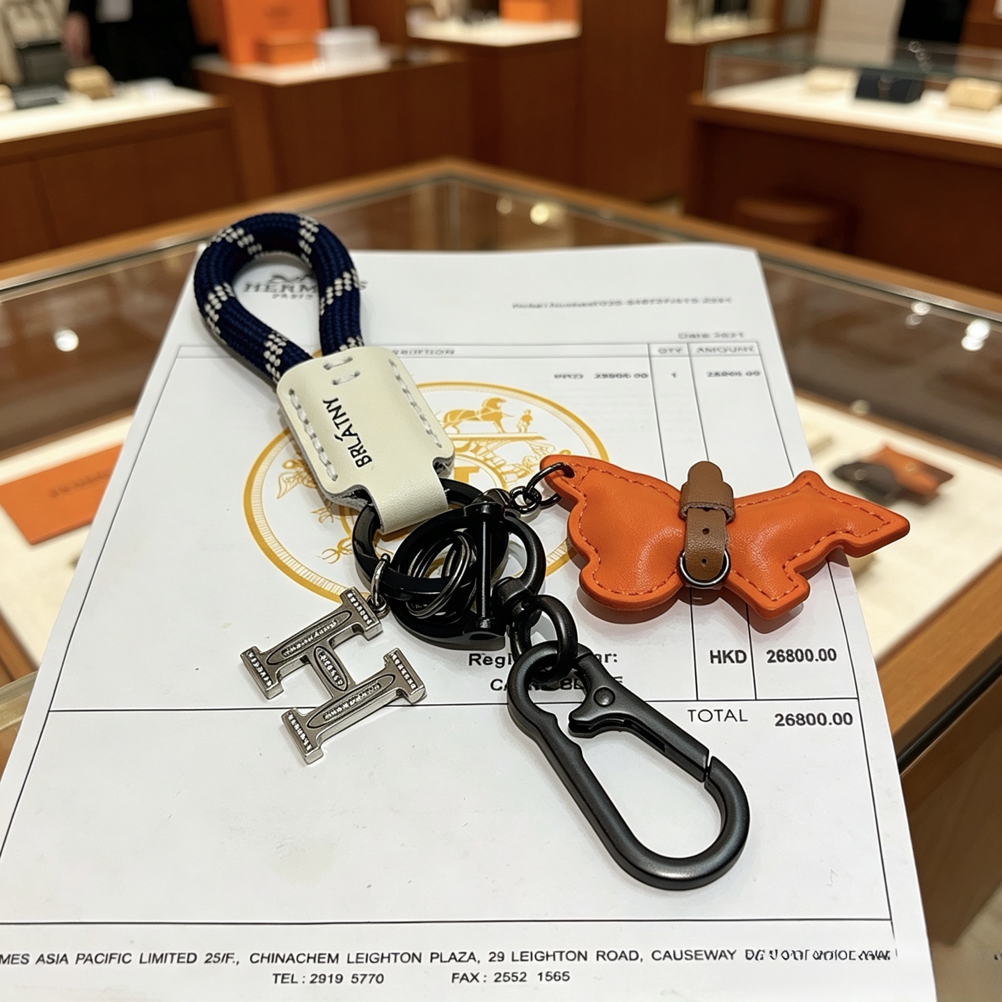 Hermes BRLATNY Puppy H Charm Keychain pendant Gunmetal hardware navy blue with white check woven strap off-white leather tag orange leather puppy charm with brown leather collar clear crystal accents on H charm 10cm total length