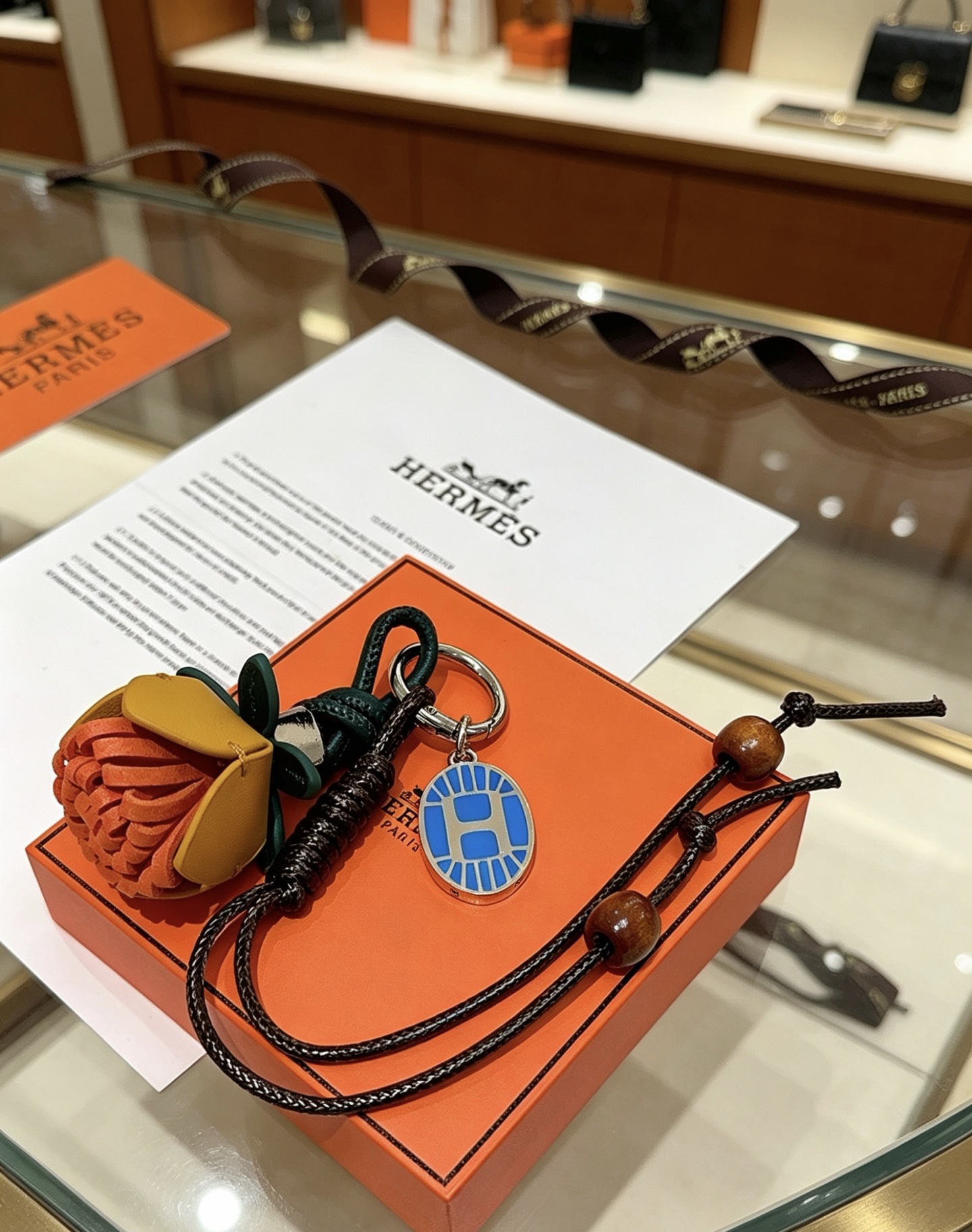 Hermes Protea Flower Charm Keychain pendant Silver-tone metal with blue enamel multi-tone leather orange mustard yellow dark green black braided cord brown wooden beads 12cm total lanyard length