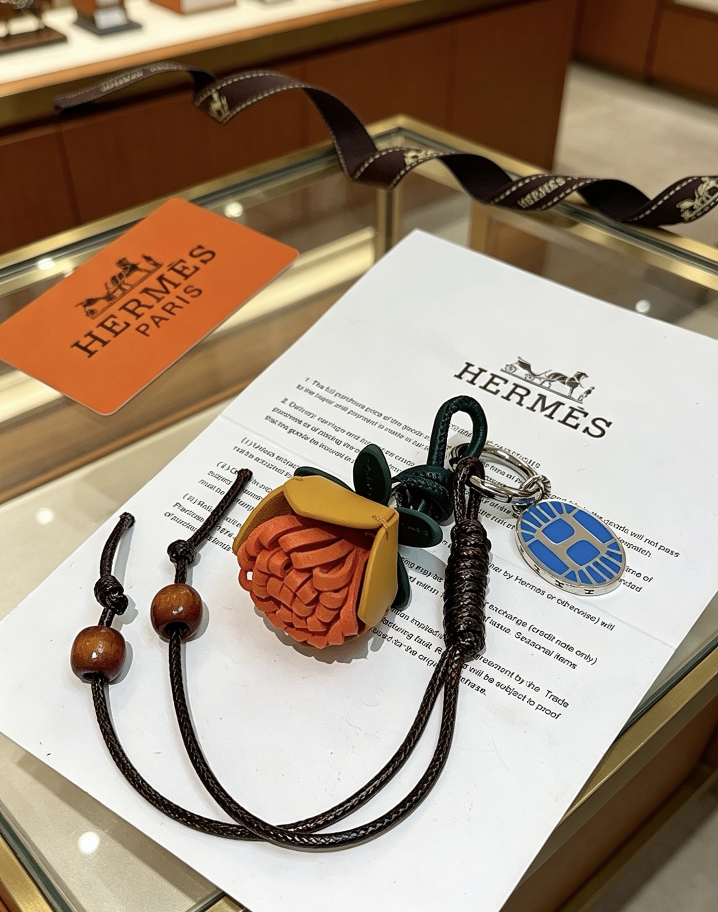 Hermes Protea Flower Charm Keychain pendant Silver-tone metal with blue enamel multi-tone leather orange mustard yellow dark green black braided cord brown wooden beads 12cm total lanyard length