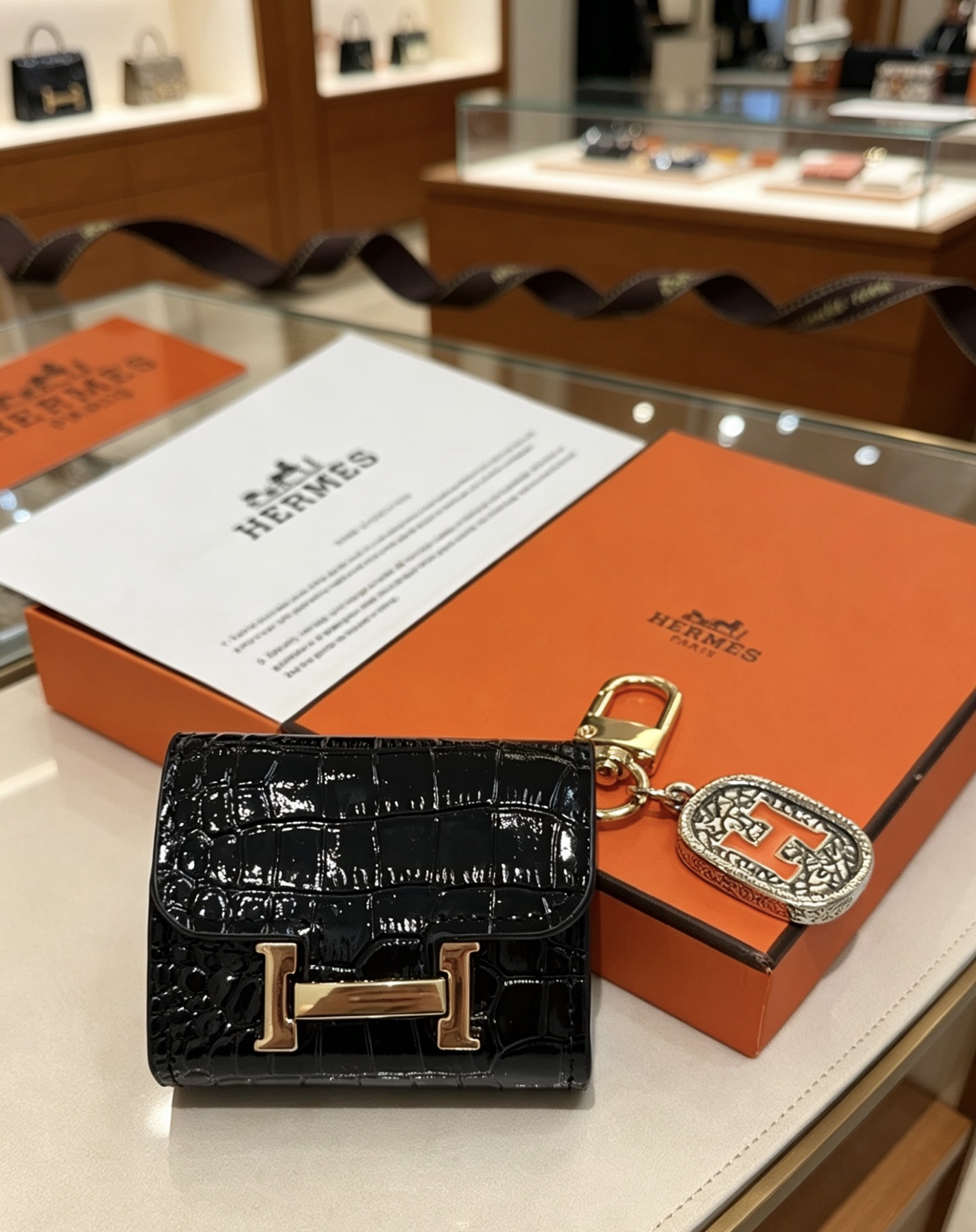 Hermes Constance AirPods Case Bag Charm pendentif Cuir verni noir embossé crocodile Quincaillerie en métal doré Charme en métal argenté avec émail orange Détail H Taille unique pour le charme AirPods standard longueur totale environ 8 cm