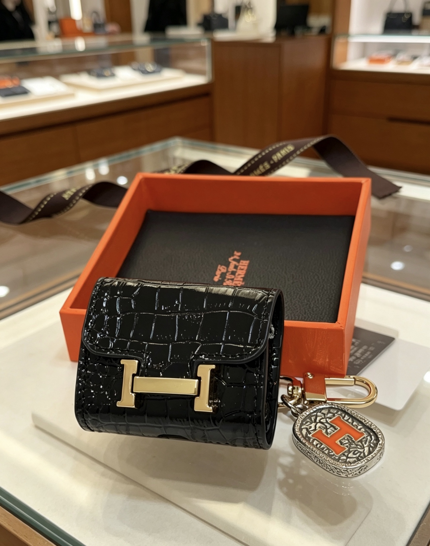 Hermes Constance AirPods Case Bag Charm pendentif Cuir verni noir embossé crocodile Quincaillerie en métal doré Charme en métal argenté avec émail orange Détail H Taille unique pour le charme AirPods standard longueur totale environ 8 cm
