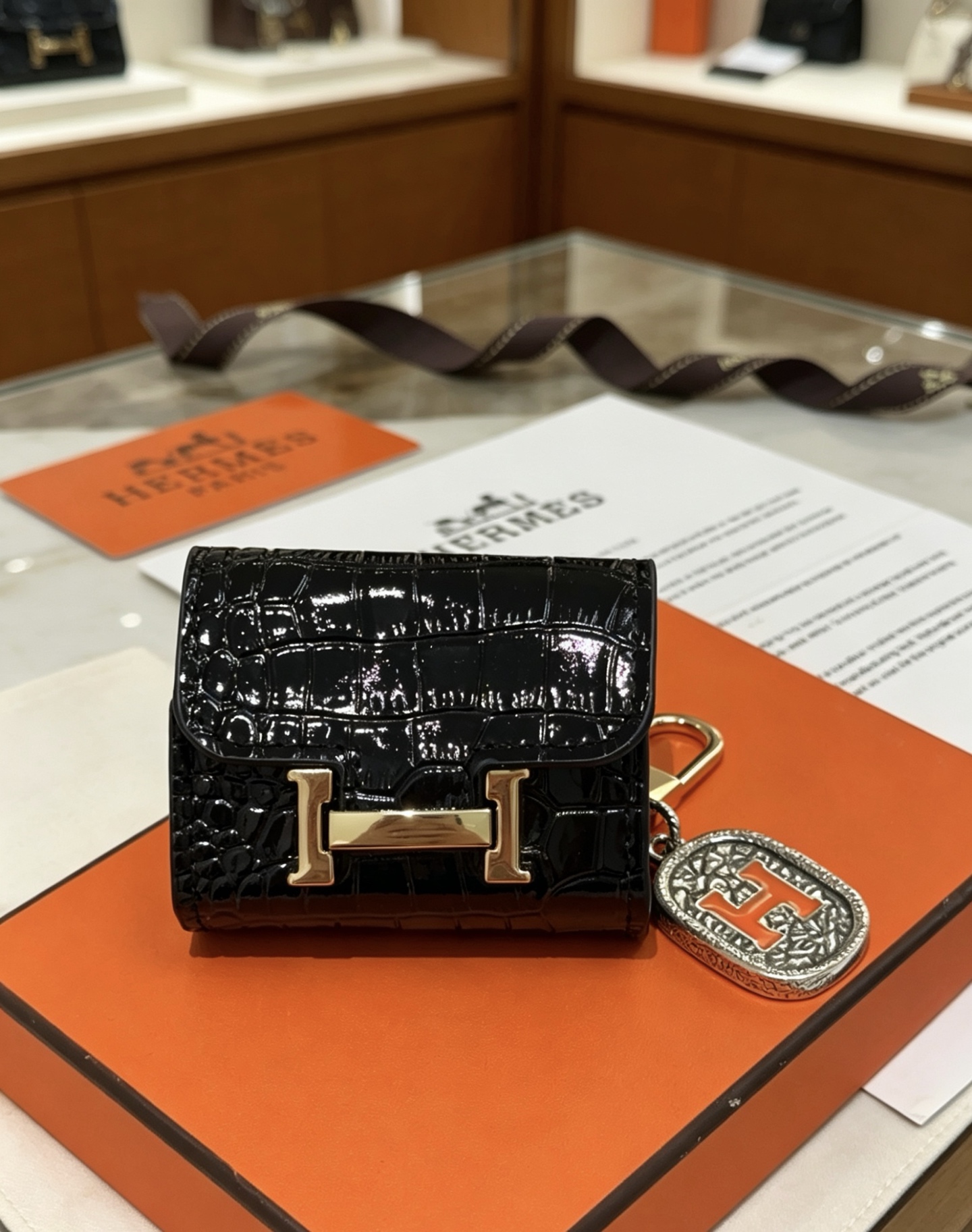 Hermes Constance AirPods Case Bag Charm pendentif Cuir verni noir embossé crocodile Quincaillerie en métal doré Charme en métal argenté avec émail orange Détail H Taille unique pour le charme AirPods standard longueur totale environ 8 cm