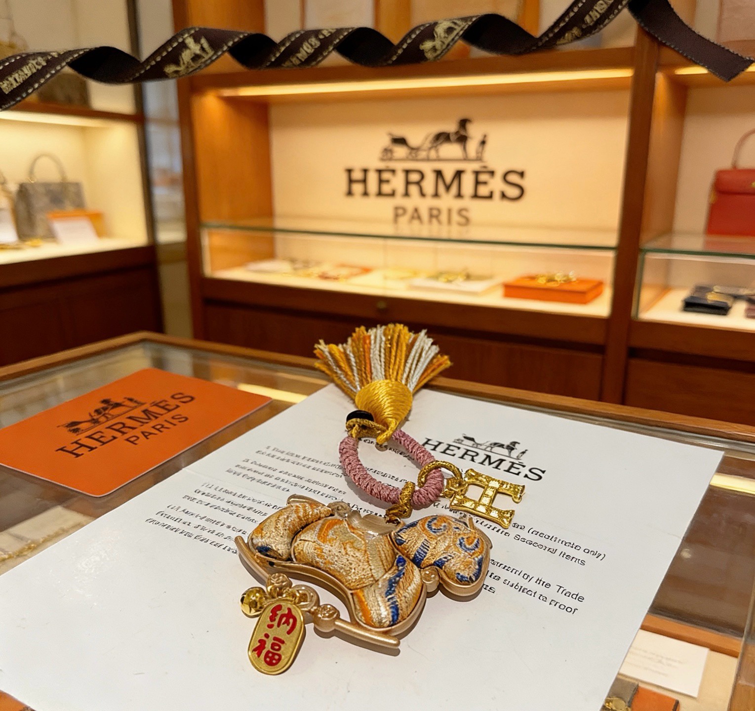 Pendentif porte-clés avec breloque cheval du Nouvel An chinois Hermes Métal doré Cordon tressé rose doré et pompon orange et blanc Tissu doré avec broderie bleue Breloque texte en émail rouge Longueur totale 12 cm