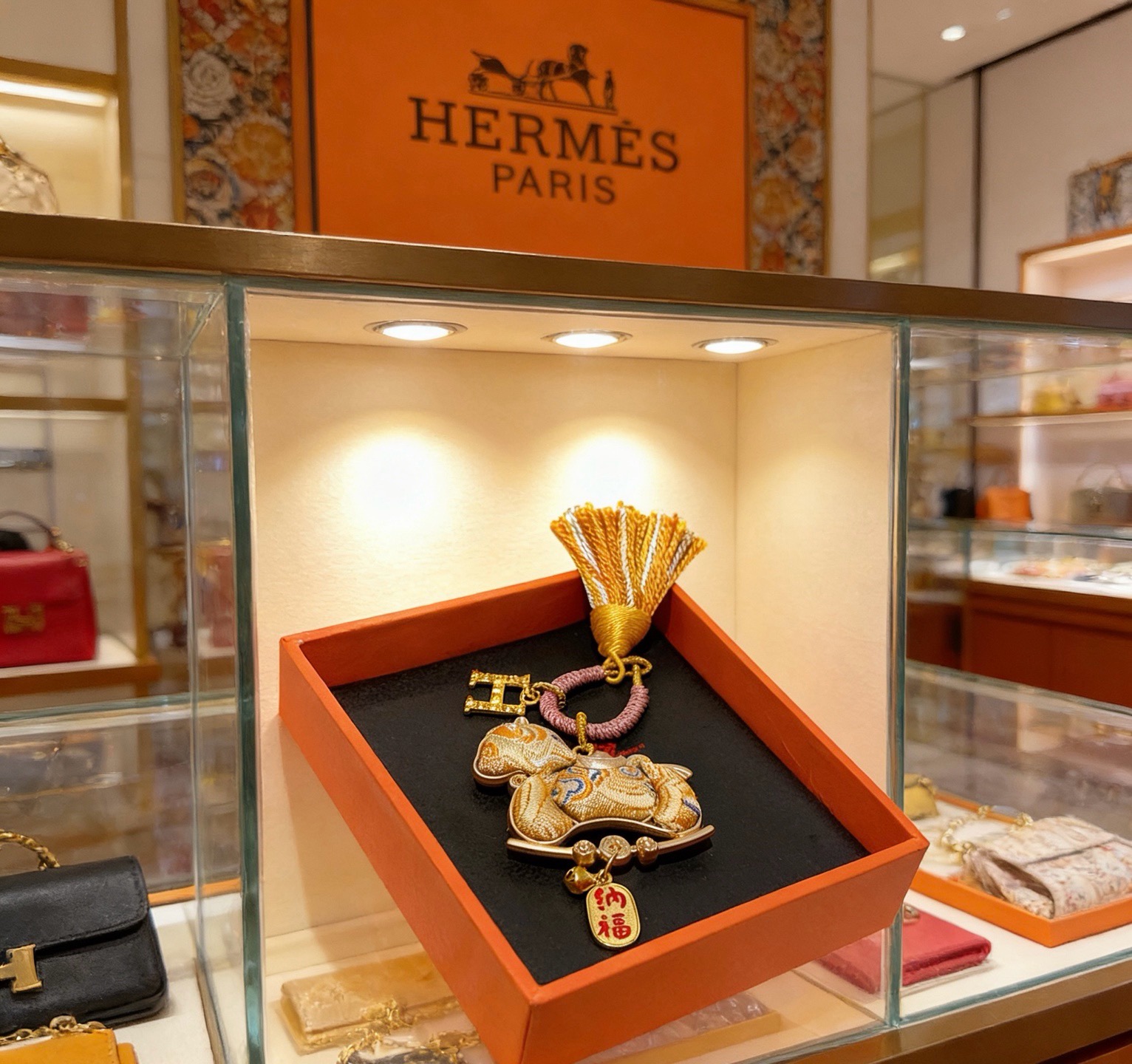 Pendentif porte-clés avec breloque cheval du Nouvel An chinois Hermes Métal doré Cordon tressé rose doré et pompon orange et blanc Tissu doré avec broderie bleue Breloque texte en émail rouge Longueur totale 12 cm