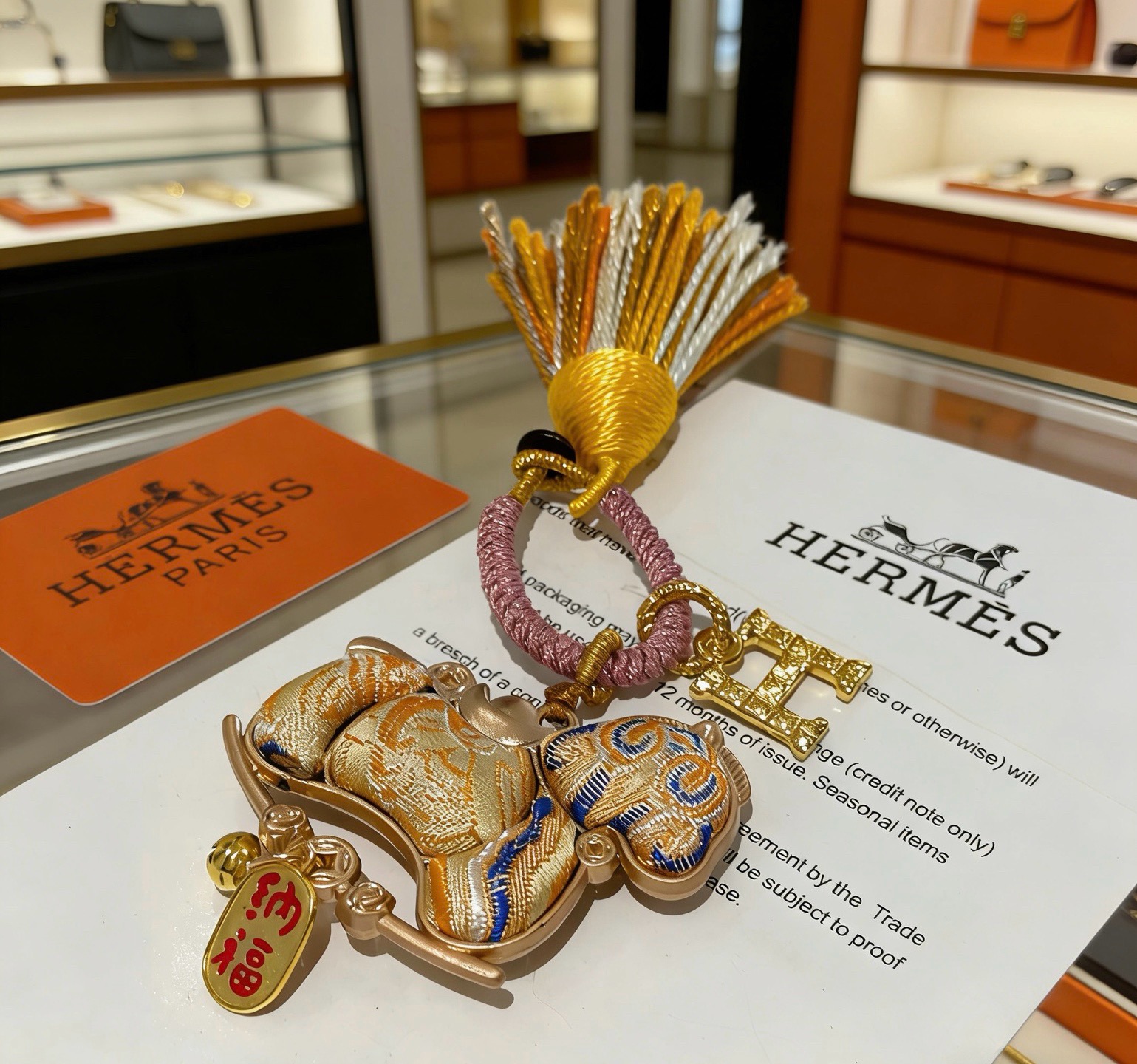 Pendentif porte-clés avec breloque cheval du Nouvel An chinois Hermes Métal doré Cordon tressé rose doré et pompon orange et blanc Tissu doré avec broderie bleue Breloque texte en émail rouge Longueur totale 12 cm
