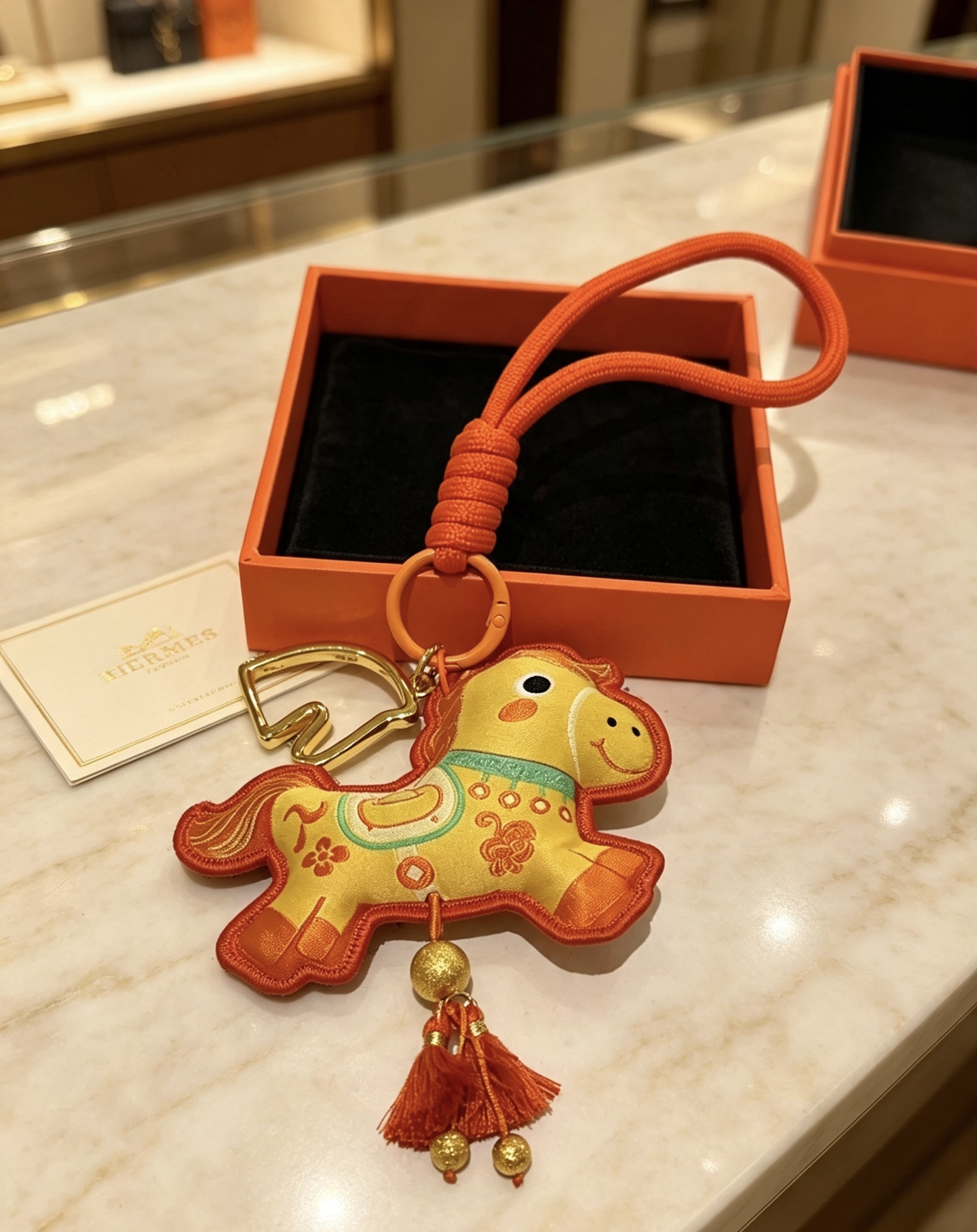 Hermes Año del caballo Colgante Lucky Horse Charm Metal en tono dorado Tela amarilla Tela y ribete naranja Detalles bordados en turquesa Borlas naranjas Longitud de la correa para la muñeca 18 cm