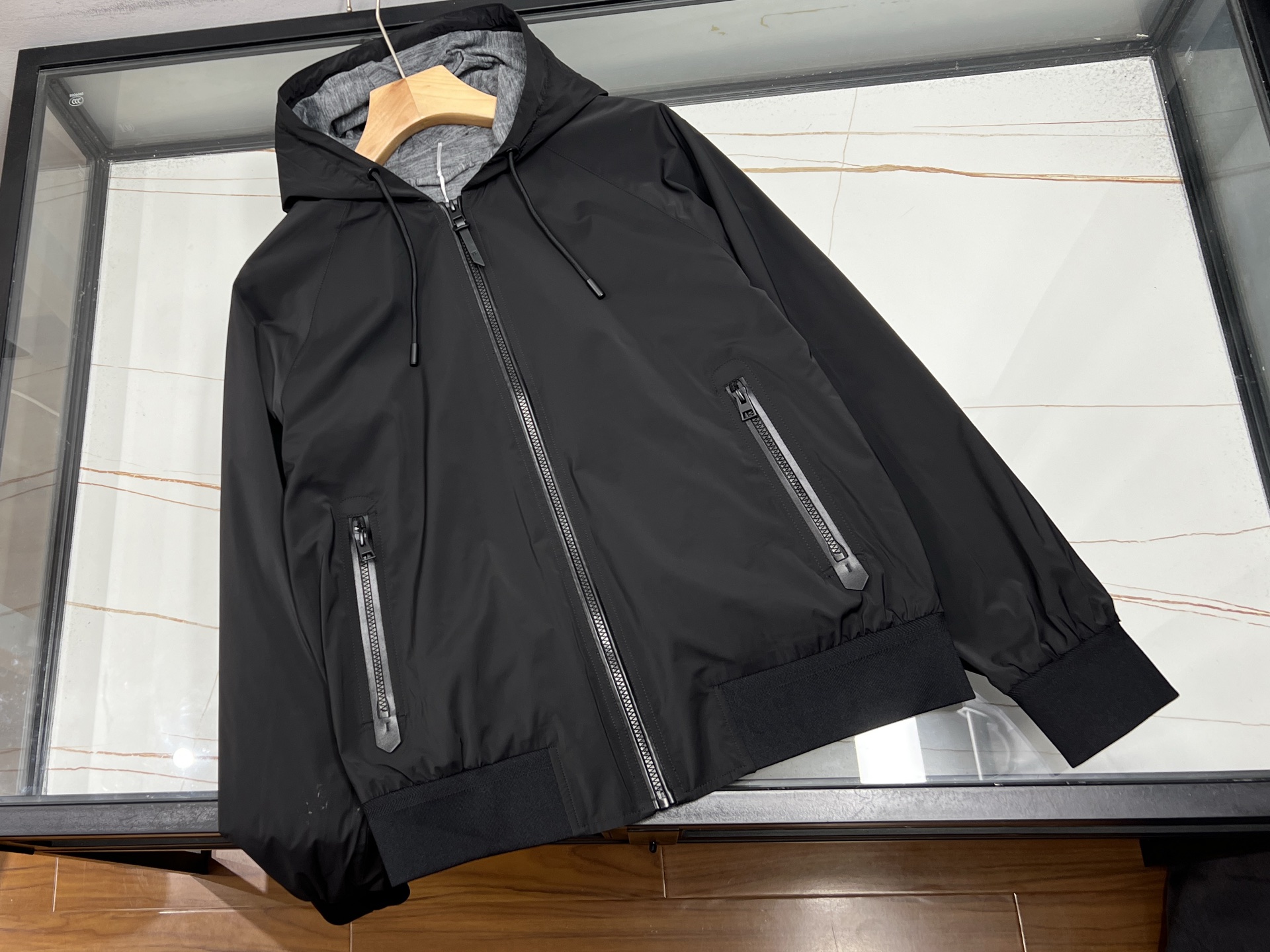 NO:722846,-26SS——TF hooded jacket is a lightweight and textured choice for spring and summer. It uses a full color design and light material to balance function and style.  The fabric and inner and outer fabrics are made of polyester fiber Solona three-proof fabric, which not only achieves windproof, waterproof, and anti-fouling functions, but also maintains the lightness and breathability required in spring and summer, and has a delicate touch without being heavy. The inner body is made of 30 wool floral gray knitted material treated with lightweight technology, which is warm and skin-friendly and moisture-wicking. With polyester fiber sleeves, the overall wear is light and burden-free, adapting to the temperature difference between day and night in spring and summer and the needs of multiple scenes.  The design details are designed in full color - the fabric, placket patchwork, and resin zippers are all in the same color, giving a simple and advanced look; the selection of resin zippers not only fits the lightweight positioning, but also blends with the overall style; the zipper pockets on both sides are matched with leather goods and accessories of the same color  The hand-oiled edges combine durability and sophistication; the hooded drawstring is flexibly adjustable, and knitted wool is used in the hood to provide light warmth; the knitted threaded edges on the hem and cuffs fit the body shape without being cramped, enhancing the windproof effect while ensuring freedom of movement.  Wearing scene: morning commute, city stroll or early summer light outdoor. It can be worn with T-shirts or shirts. It can not only cope with the changing climate of spring and summer, but also create a simple and advanced daily style with a neat silhouette. It is a core item in the spring and summer wardrobe that is both light, comfortable and practical. Black 48-56, men's clothing, tom ford, jackets & coats, shirts, tees, t-shirts, hats,19860909-26SS———TF连帽夹克,是春夏轻量穿搭的质感之选,以全顺色设计与轻薄材质,平衡功能与格调.  面料与内里外层面料选用聚酯纤维索罗娜三防面料,在实现防风、防水、防污功能的同时,保持春夏所需的轻薄透气,触感细腻无厚重感；内里大身采用轻量化工艺处理的30羊毛花灰色针织材质,温润亲肤且吸湿排汗,配合聚酯纤维袖里,整体穿着轻盈无负担,适配春夏昼夜温差与多场景需求. 设计细节采用全顺色设计——面料、门襟拼皮、树脂拉链均统一色调,视觉简约高级；树脂拉链的选用既契合轻量化定位,又与整体风格相融；两侧拉链口袋搭配同色系皮件与手工油边,耐用性与精致感兼具；连帽抽绳可灵活调节,帽里同步采用针织羊毛延续轻暖；下摆与袖口的针织螺纹收边,贴合身形且不局促,强化防风效果的同时保障活动自由. 穿着场景晨间通勤、城市漫步或初夏轻户外,内搭T恤、衬衫皆可,既能应对春夏多变气候,又能以利落版型塑造简约高级的日常风格,是春夏衣橱中轻薄舒适与实用型格兼具的核心单品. 现货发售黑色48-56,男装,tom ford,jackets & coats,shirts,tees，t-shirt,hats,,Women's clothing