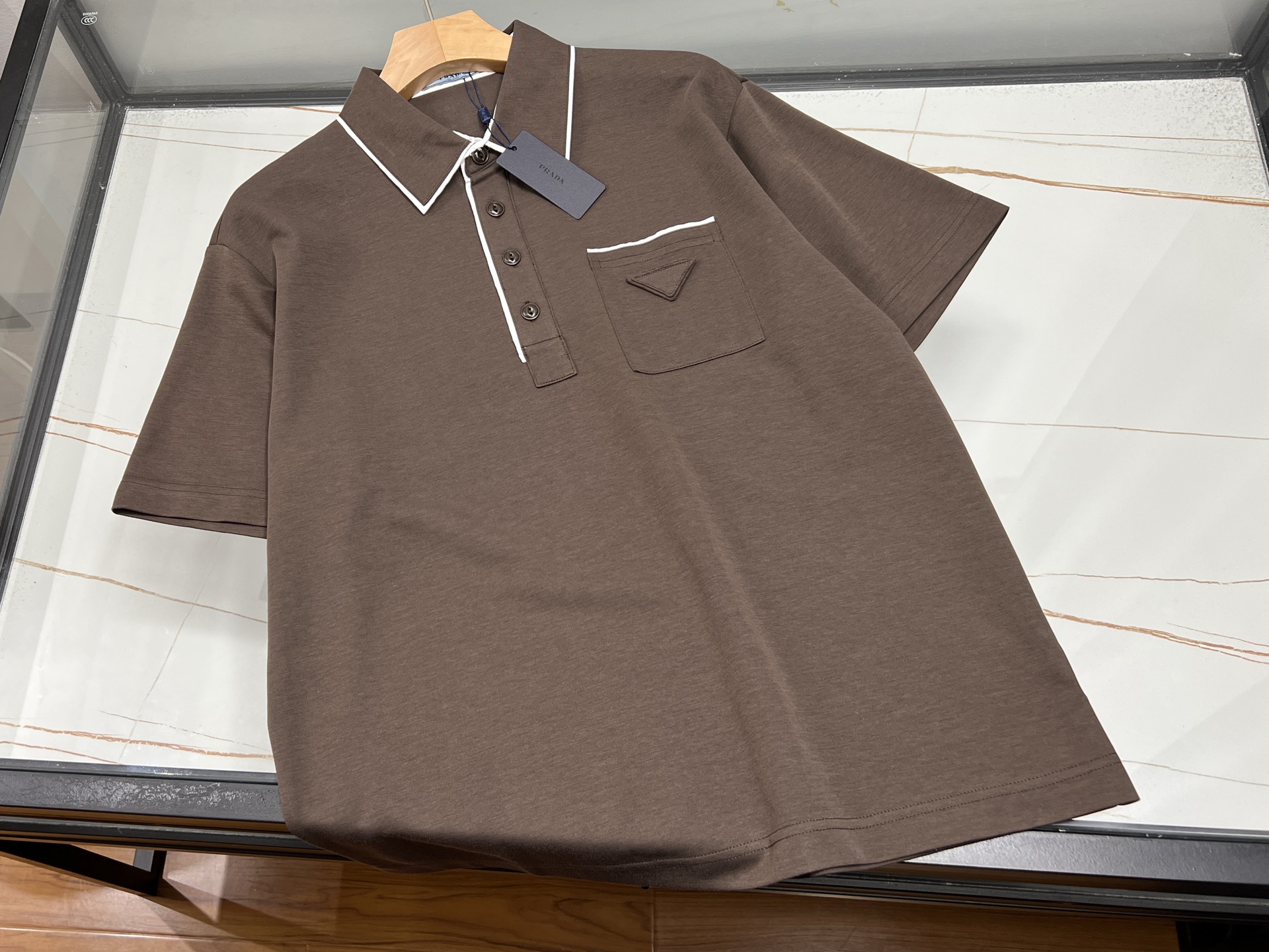 NO:785963,-26SS——Simple and fashionable, unlocking a new style of summer wear. This short-sleeved T-shirt perfectly combines simplicity and fashion. The classic lapel design is neat and spirited, easily breaking the monotony of the traditional round collar, adding a sense of sophistication and sophistication to the overall look. The unique triangle logo on the chest is the finishing touch, simple yet individual, showing your unique taste in a low-key manner, making you stand out from the crowd. The short-sleeved style is refreshing and comfortable, very suitable for hot summer wear.  The fabric is skin-friendly and breathable, comfortable and unburdened when worn close to the body, and allows you to move freely without restriction. Whether you wear it with casual pants for a stroll on the street, or with suit pants for casual business occasions, it can be easily controlled and create different styles of fashion for you. It is an indispensable and versatile item in your summer wardrobe. Available in stock in two colors S-XXL, Prada-clothing, prada, T-shirt, tees, t-shirt, business suit,19860909-26SS———简约时尚,解锁夏日穿搭新风尚 这款短袖T恤,将简约与时尚完美融合.经典翻领设计,利落又精神,轻松打破传统圆领的单调感,为整体造型增添一份精致与干练. 胸前独特的三角标是点睛之笔,简约而不失个性,在低调中彰显独特品味,让你在人群中脱颖而出.短袖款式,清爽自在,非常适合炎炎夏日穿着. 面料亲肤透气,贴身穿着舒适无负担,活动自如不受限.无论是搭配休闲裤漫步街头,还是配上西装裤出席轻松商务场合,它都能轻松驾驭,为你打造出不同风格的时尚造型,是夏日衣橱里不可或缺的百搭单品. 现货发售二色S-XXL,普拉达-服装,prada,T-shirt,tees，t-shirt,business suit,,Women's clothing