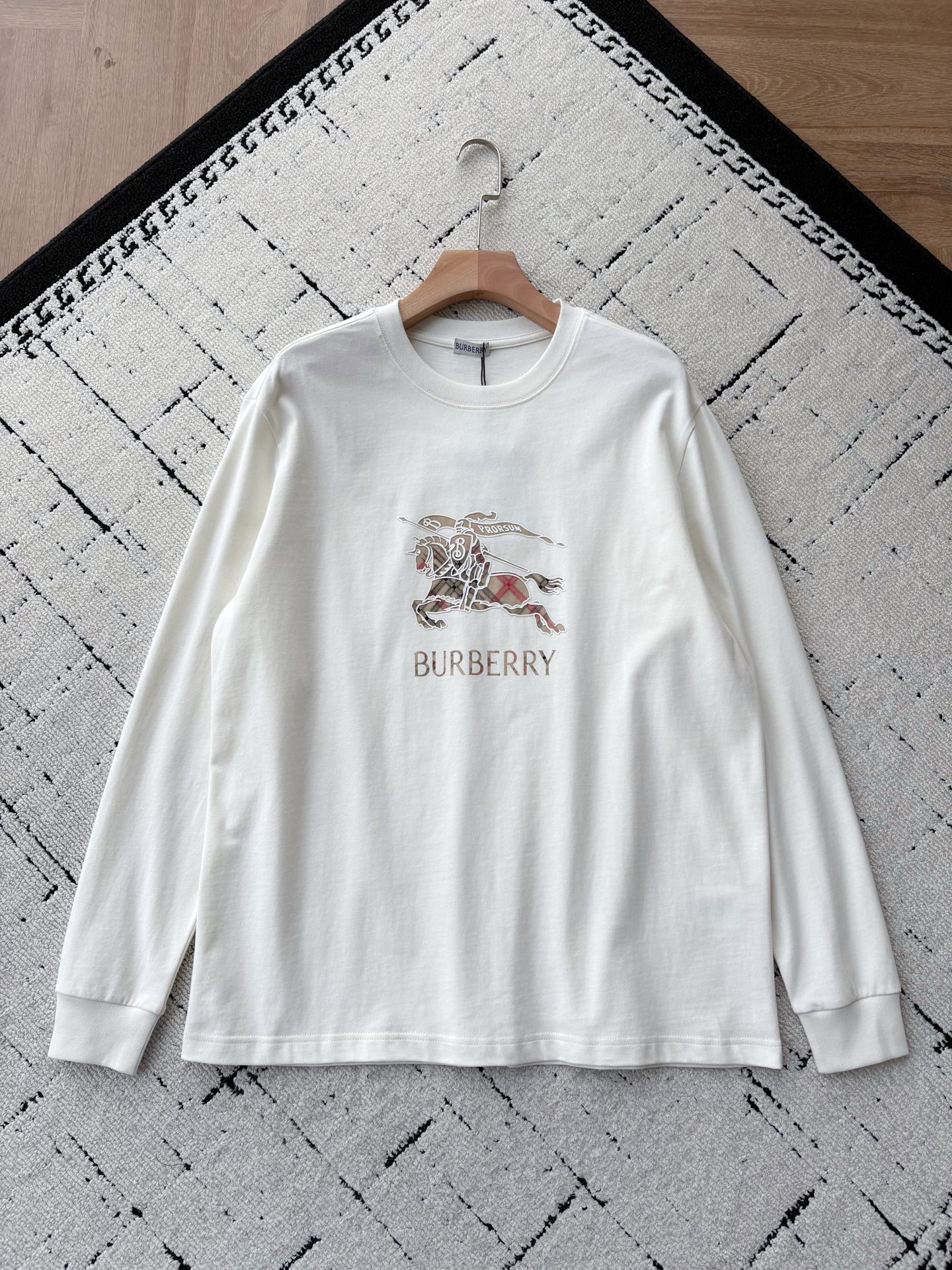 NO:656730,BBR British Knight Classic Plaid Long-Sleeved White T-shirt This pure white long-sleeved T-shirt condenses BUR**'s classic elements into daily wear, creating a timeless item with both texture and recognition. The iconic badge shows off the style. The exquisite 'Knight War Horse and PRORSUM Flag' badge on the chest is filled with the brand's iconic plaid pattern, cleverly integrating the core symbols of the brand. Every embroidery detail shows exquisite craftsmanship.  We select skin-friendly cotton materials for comfort and travel. We use 99% pure cotton fabric, which is soft to the touch, skin-friendly and breathable. The exquisite stitching technology and moderate weight ensure a crisp and stylish silhouette and long-term wearing comfort, making it an ideal choice for daily matching.  Simple silhouette, versatile classic round neck design, and loose straight fit. Whether worn alone to show the badge pattern, or worn as an inner layer to reveal the exquisite gray brand label on the collar, it can be easily integrated into different styles, presenting a simple but not simple style. Same style for men and women, white, XS-L sizes. 1-3CM error in flat measurement  M code: Shoulder width 51 Bust 122 Length 78 Sleeves 68 L code: Shoulder width 52 Bust 126 Length 80 Sleeves 69 Girls choose XS code; boys below 135 pounds choose XS code; 135-155 pounds choose S code; 155-175 pounds choose M code; 175-190 pounds choose L code.,,burberry,tees,t-shirt,alexander wang19860909BBR英伦骑士 经典格纹长袖白T恤 这款纯白长袖T恤,将BUR**的经典元素浓缩于日常穿搭之中,打造兼具质感与辨识度的永恒单品. 标志性徽章,尽显风范胸前精致的“骑士战马与PRORSUM旗帜”徽章,以品牌标志性格纹填充,巧妙融合品牌的核心符号.每一处刺绣细节都展现了精湛工艺. 甄选亲肤棉料,舒适随行采用99纯棉面料,触感柔软且亲肤透气.考究的缝线工艺与适中的克重,确保了挺括有型的廓感与长久穿着的舒适度,是日常搭配的理想之选. 简约廓形,百搭经典经典的圆领设计,配合宽松直筒版型,无论是单穿展现徽章图案,还是作为内搭露出领口精致的灰色品牌标签,都能轻松融入不同风格,呈现简约而不简单的格调. 男女同款,白色,XS-L码. 平铺测量1-3CM误差 XS码:肩宽49胸围114衣长74袖子66 S码:肩宽50胸围118衣长76袖子67 M码:肩宽51胸围122衣长78袖子68 L码:肩宽52胸围126衣长80袖子69 女生选择XS码； 男生 135斤以下选择XS码；135-155斤选择S码； 155-175斤选择M码；175-190斤选择L码.,,burberry,tees，t-shirt,alexander wang,Men's clothing