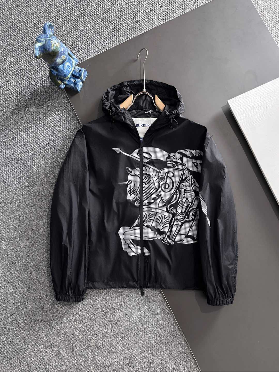 NO:528785,Burber Equestrian Knight Logo Shock Jacket Jacket The fabric is made of high-quality nylon fabric, with lightness, LL1670350 wear resistance, windproof and waterproof, which is very suitable for making casual jackets. In the fabric treatment, special waterproof coating treatment technology is used to enhance its waterproof performance. Cut and sew the fabric into the required shape and size according to the design drawings. Use advanced sewing equipment and technology to sew the fabric together to form the overall structure of the jacket. During the sewing process, special attention is paid to details, such as sewing of zippers, pockets, cuffs, etc., to ensure its firmness and aesthetics. A very accurate restoration of logo patterns is required. Logo and printing treatment Decorate the Equestrian Knight logo (EKD) and B-shaped zipper heads on the jacket through glue printing to highlight the brand characteristics.  Printing treatment uses environmentally friendly and washable pigments to ensure that the printing is long-lasting and bright. The drawstring hood and hem design can adjust the tightness according to weather changes to provide better protection. Back-fitting and inspection The sewn jacket is processed afterwards, such as ironing, thread removal, etc., to make it more flat and beautiful. Strict quality inspection SIZE:S-XL,,burberry, jackets & coats,jackets & coats,hats,alexander wang19860909Burber马术骑士徽标 冲锋衣夹克外套 面料由高品质的尼龙面料,具有轻盈、LL1670350耐磨、防风防水等特性,非常适合制作休闲夹克. 在面料处理上,采用特殊的防水涂层处理技术,以增强其防水性能. 裁剪与缝制 根据设计图纸,将面料裁剪成所需形状和尺寸. 使用先进的缝制设备和技术,将面料缝制在一起,形成夹克的整体结构. 在缝制过程中,特别注意细节处理,如拉链、口袋、袖口等部位的缝制,确保其牢固度和美观度. 需要非常精准的还原徽标图案 徽标与印花处理 通过胶浆印花将马术骑士徽标（EKD）和B字型拉链头装饰在夹克上,彰显品牌特色. 印花处理采用环保、耐洗的颜料,确保印花持久、鲜艳. 抽绳式连帽与衣摆设计,可根据天气变化调整松紧度,提供更好的防护效果. 后整与检验 对缝制好的夹克进行后整处理,如熨烫、去线头等,使其更加平整、美观. 进行严格的质量检验 SIZE:S-XL,,burberry,jackets & coats,jackets & coats,hats,alexander wang,Men's clothing